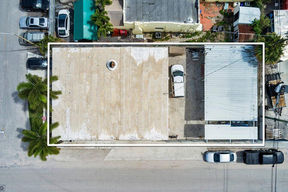 Aerial view of a large flat-roofed building outlined in white, with parked cars and streets around it.
