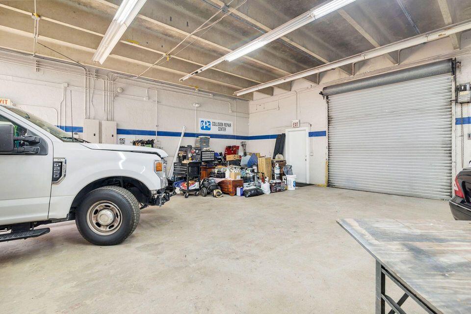 Automotive workshop with a large roll-up door, exposed ceiling beams, equipment, and a white pickup truck.
