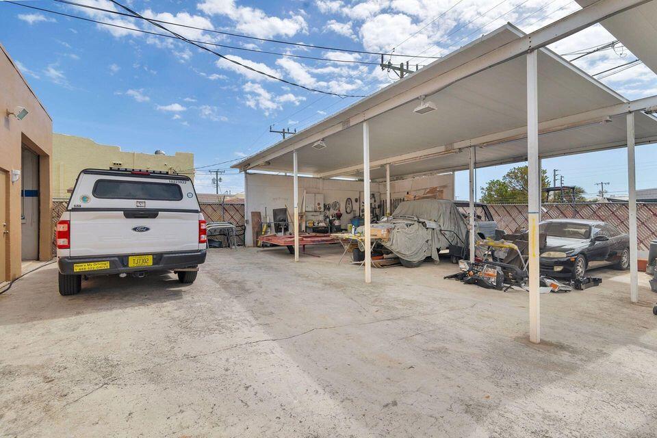 Covered vehicle work area with parked trucks and cars beneath a large metal canopy.