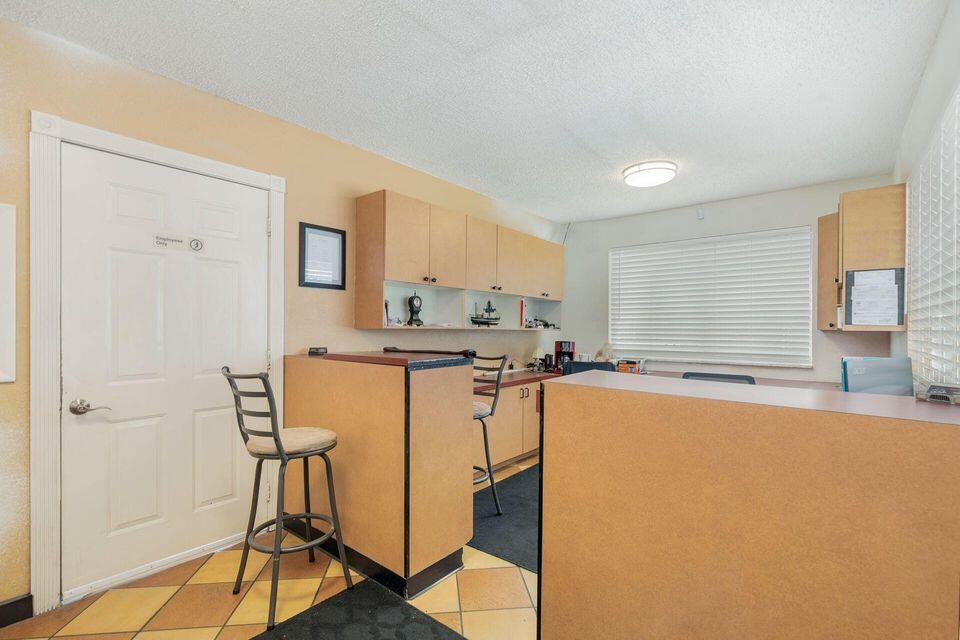 Office reception area with tan counters, tall stools, wall cabinets, and a window with closed blinds.