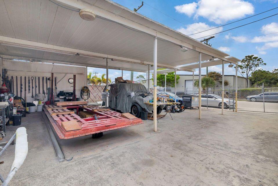 Covered workshop with a red vehicle lift, tools, and cars behind a chain-link fence.