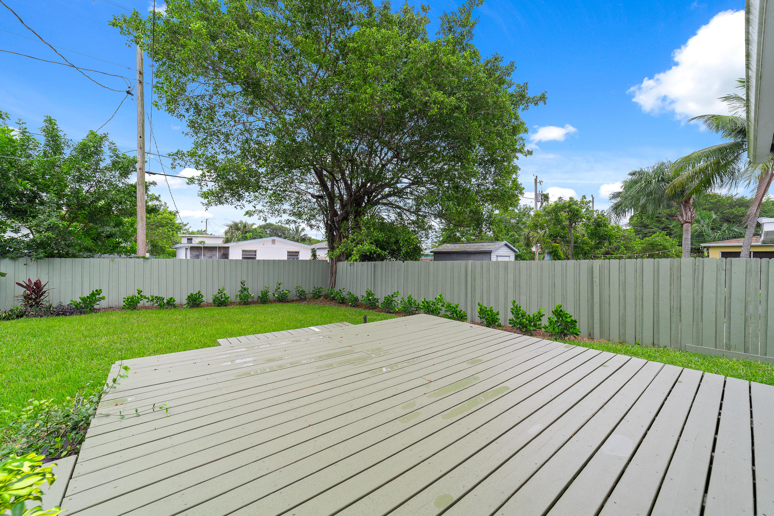 Backyard deck overlooking a fenced lawn with mature trees and tropical landscaping.