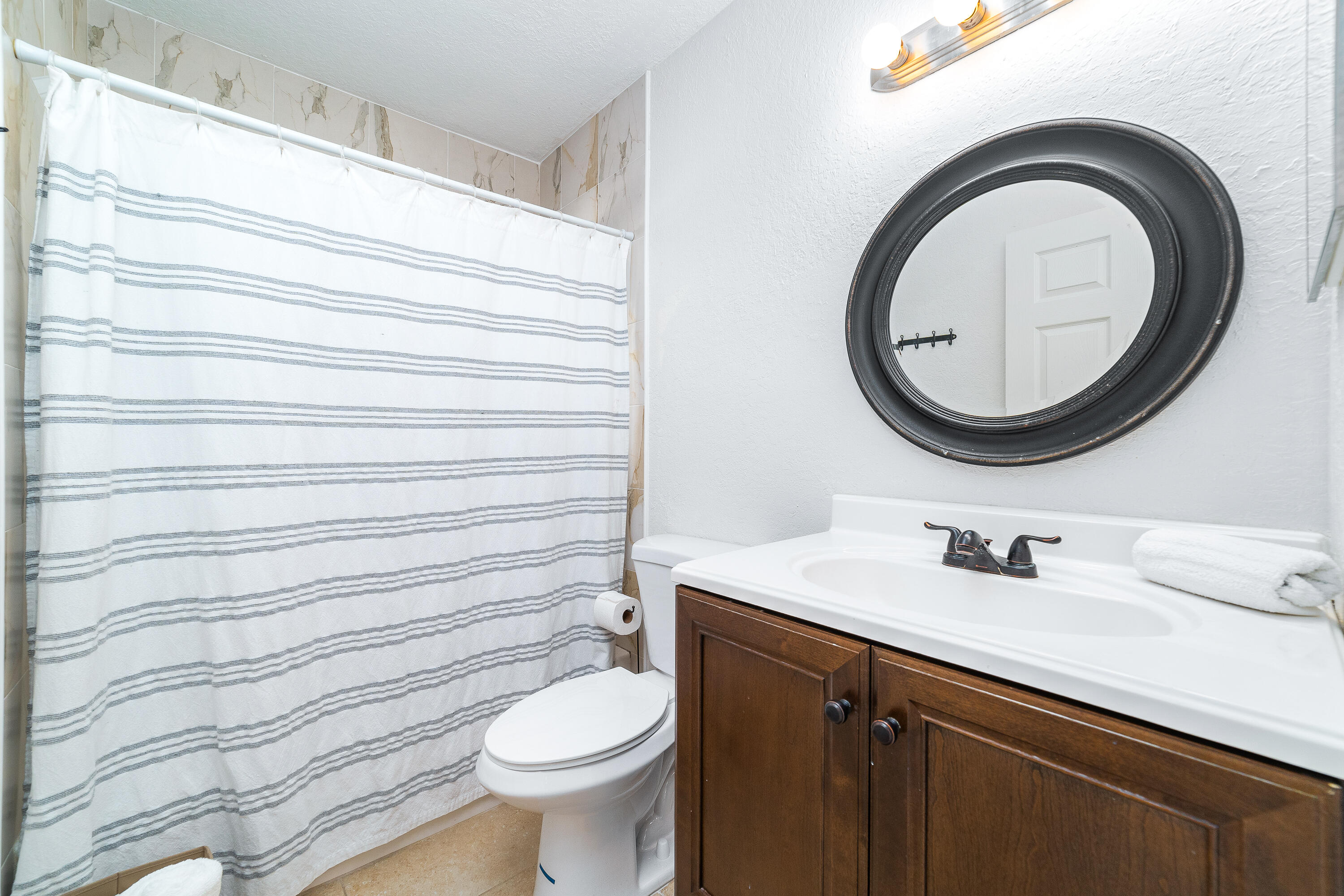 Bathroom with a striped shower curtain, dark wood vanity, and round black-framed mirror.