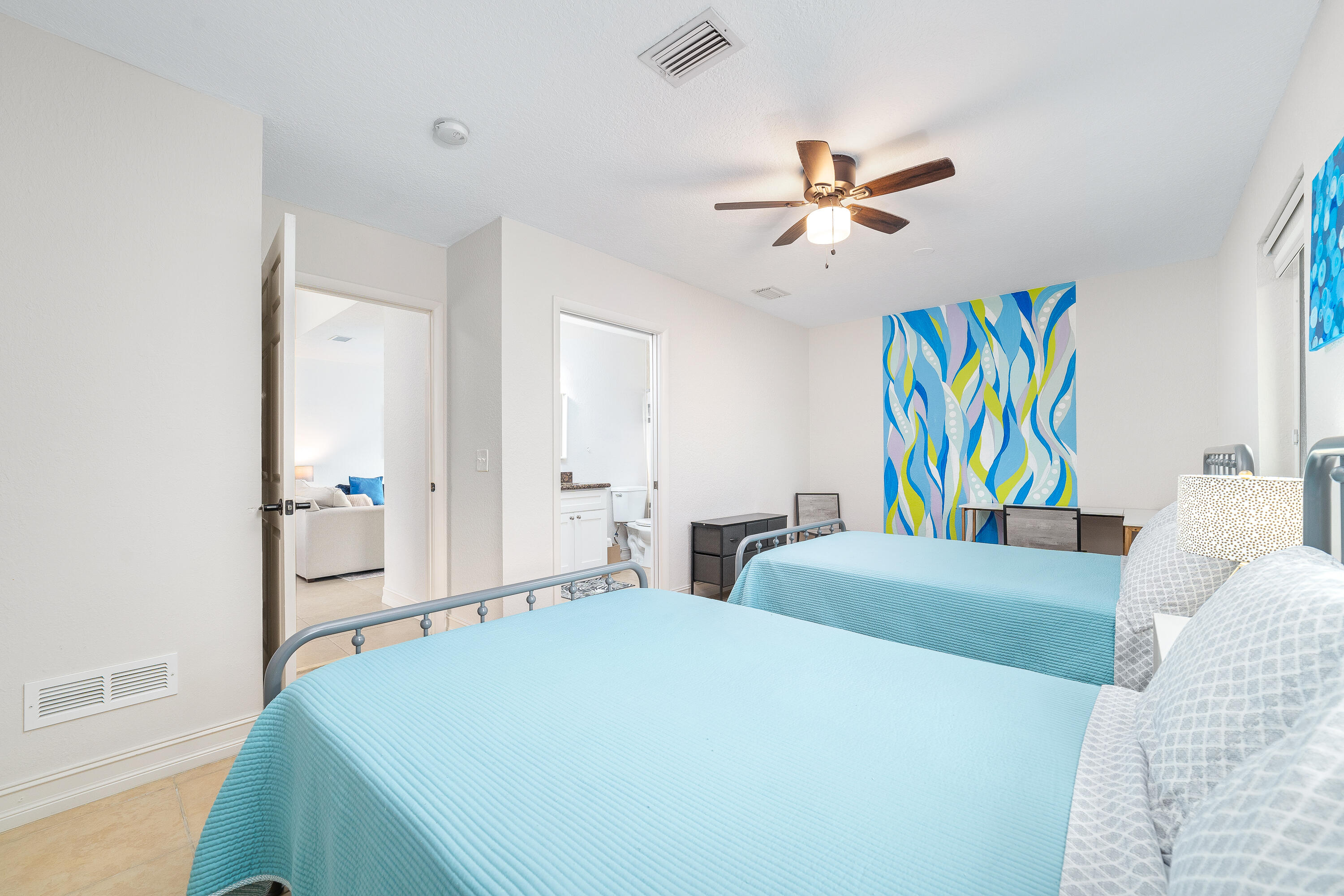 Bedroom with two turquoise-covered twin beds and a colorful abstract mural.
