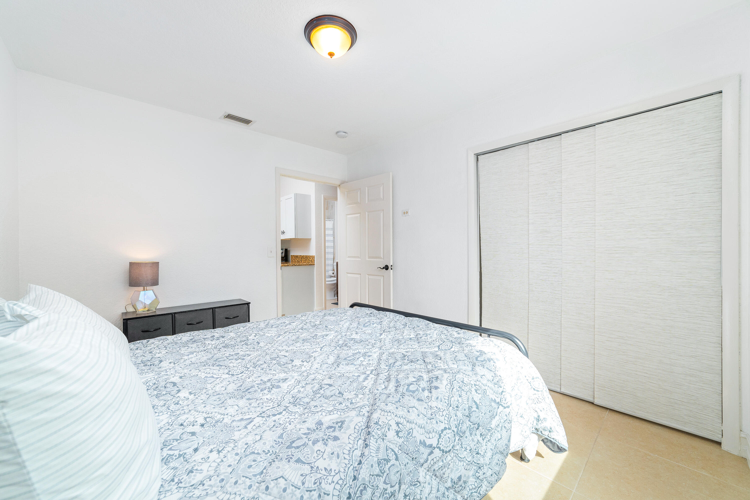 Furnished bedroom with blue-and-white patterned bedding and wide vertical blinds.