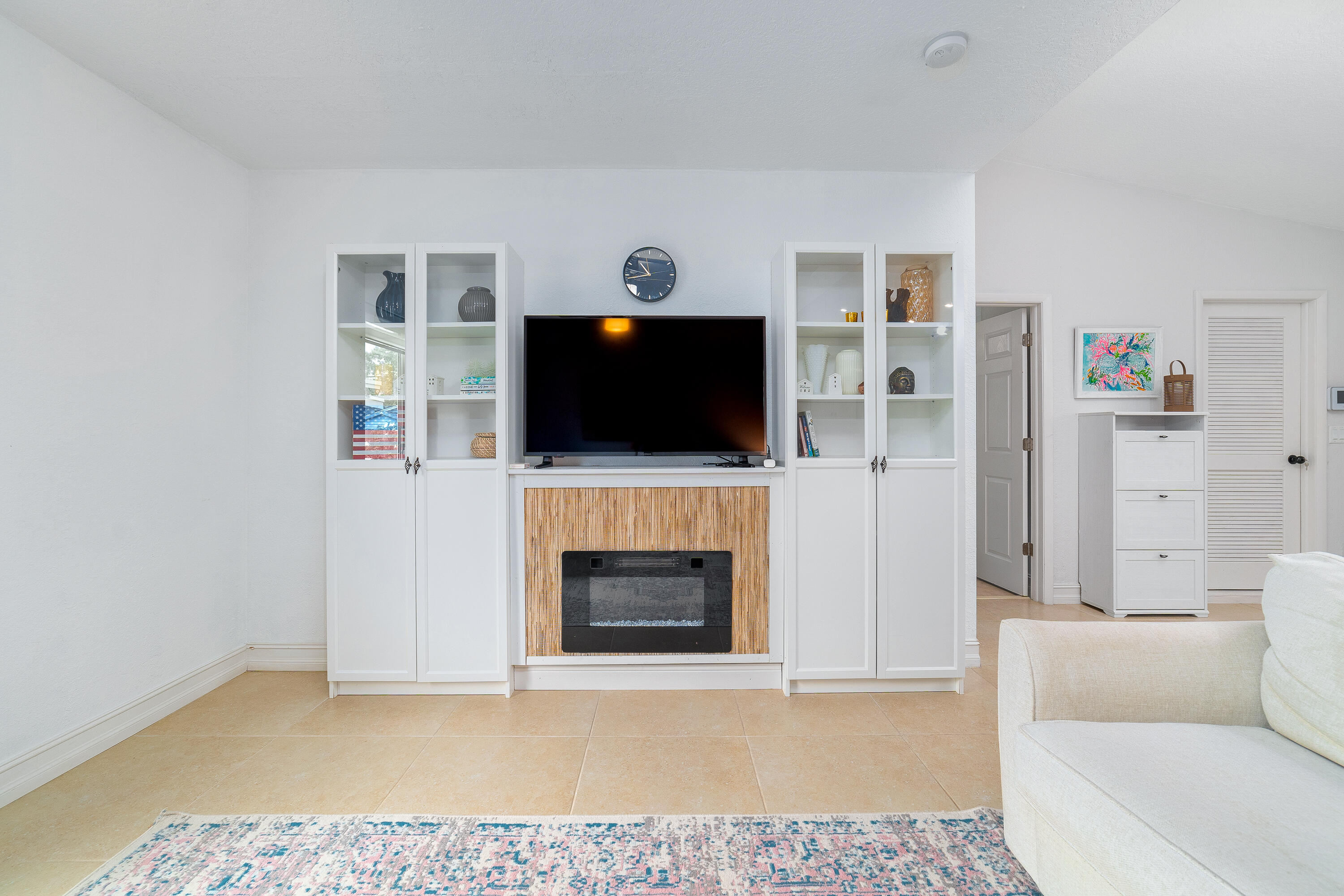 Living room with white built-ins, a television above a linear fireplace, and glass-front cabinets.