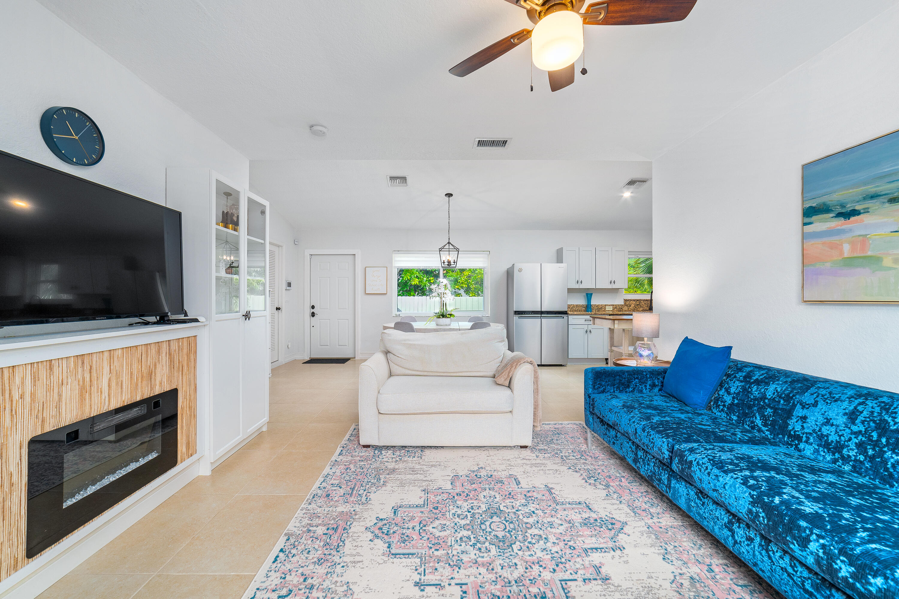 Open-plan living room with a vivid blue sofa, cream armchair, and adjacent kitchen.