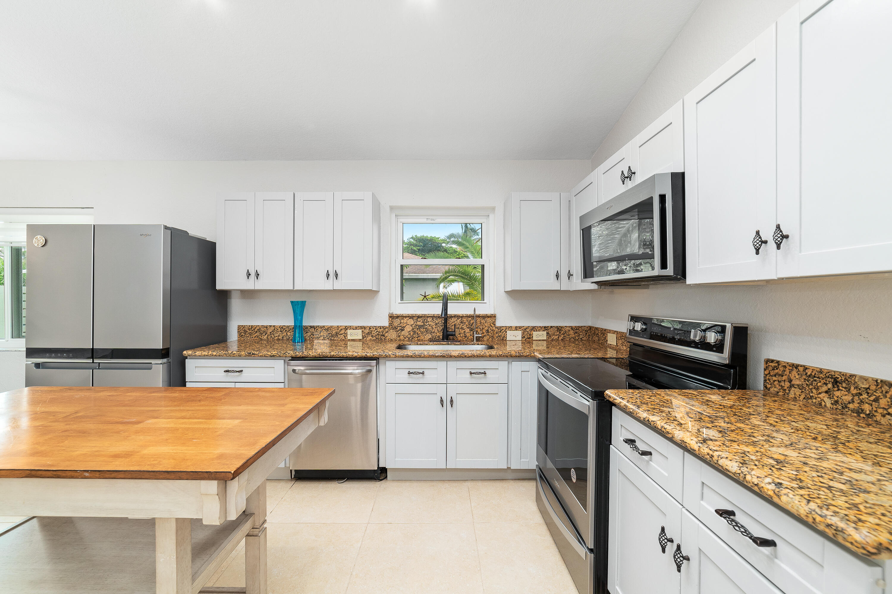 Bright kitchen with granite counters, white cabinets, stainless steel appliances, and a wooden table.