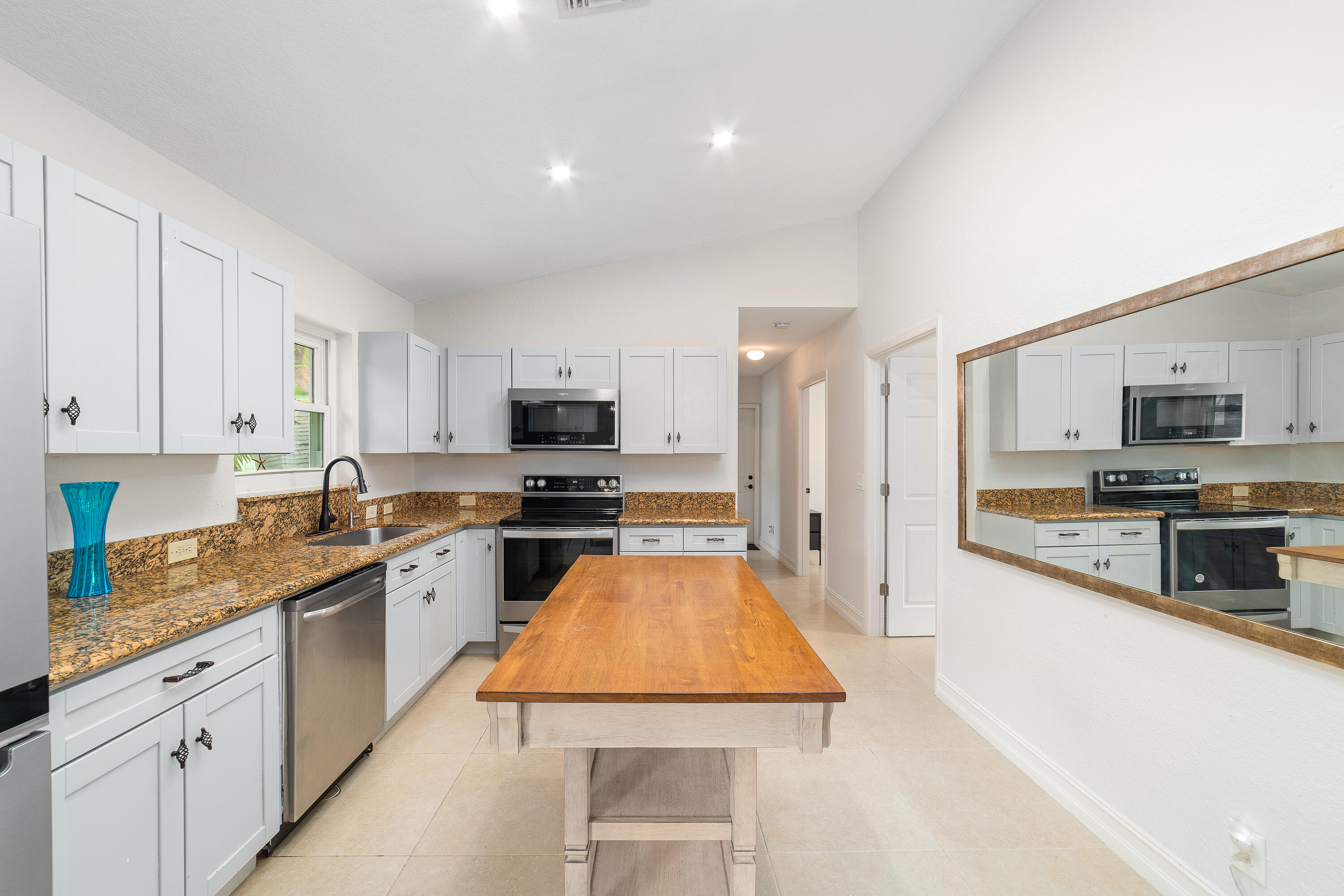 Kitchen with white cabinets, granite counters, stainless steel appliances, and a large wooden worktable.