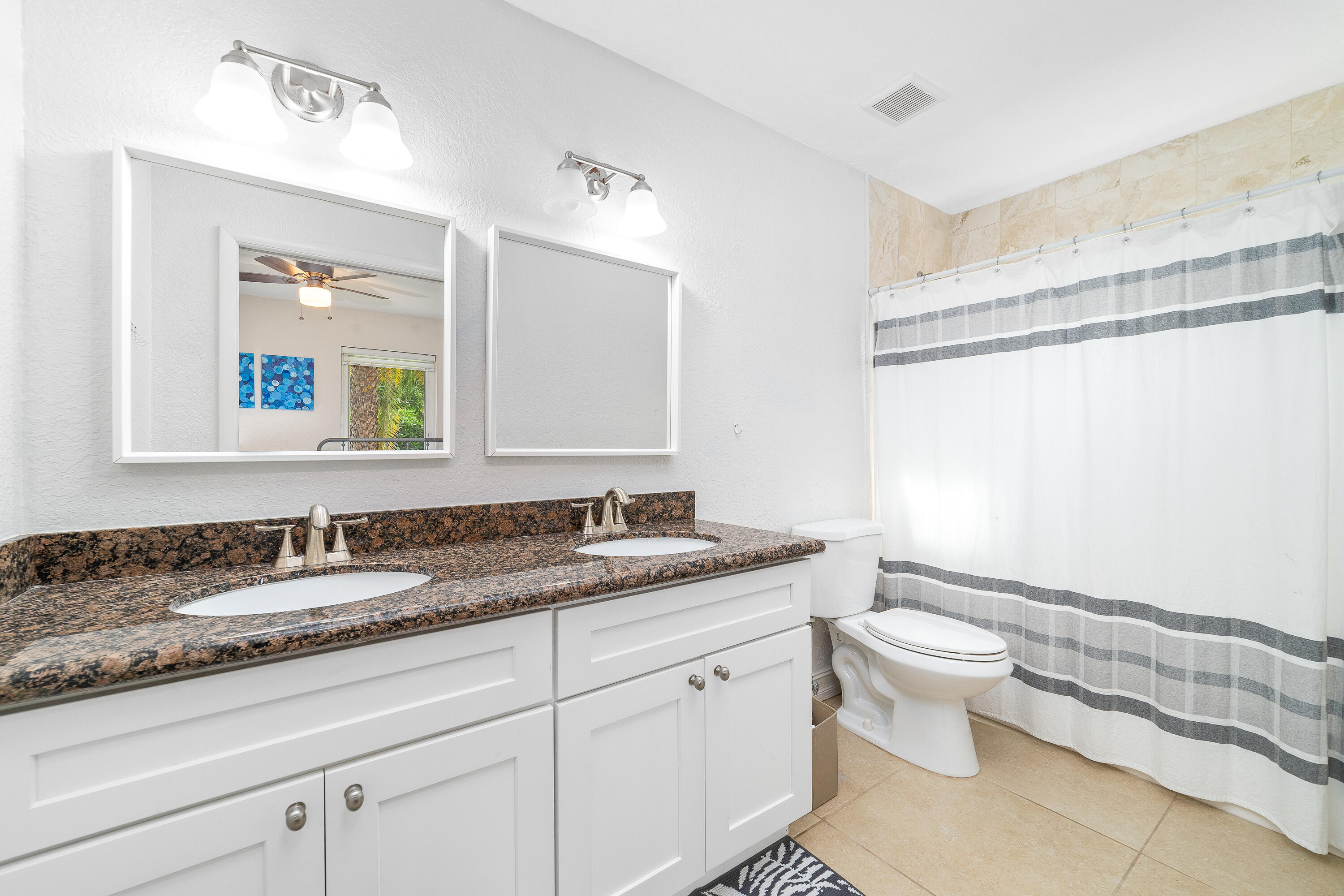 Bathroom with a double vanity, granite countertops, and a gray-striped shower curtain.