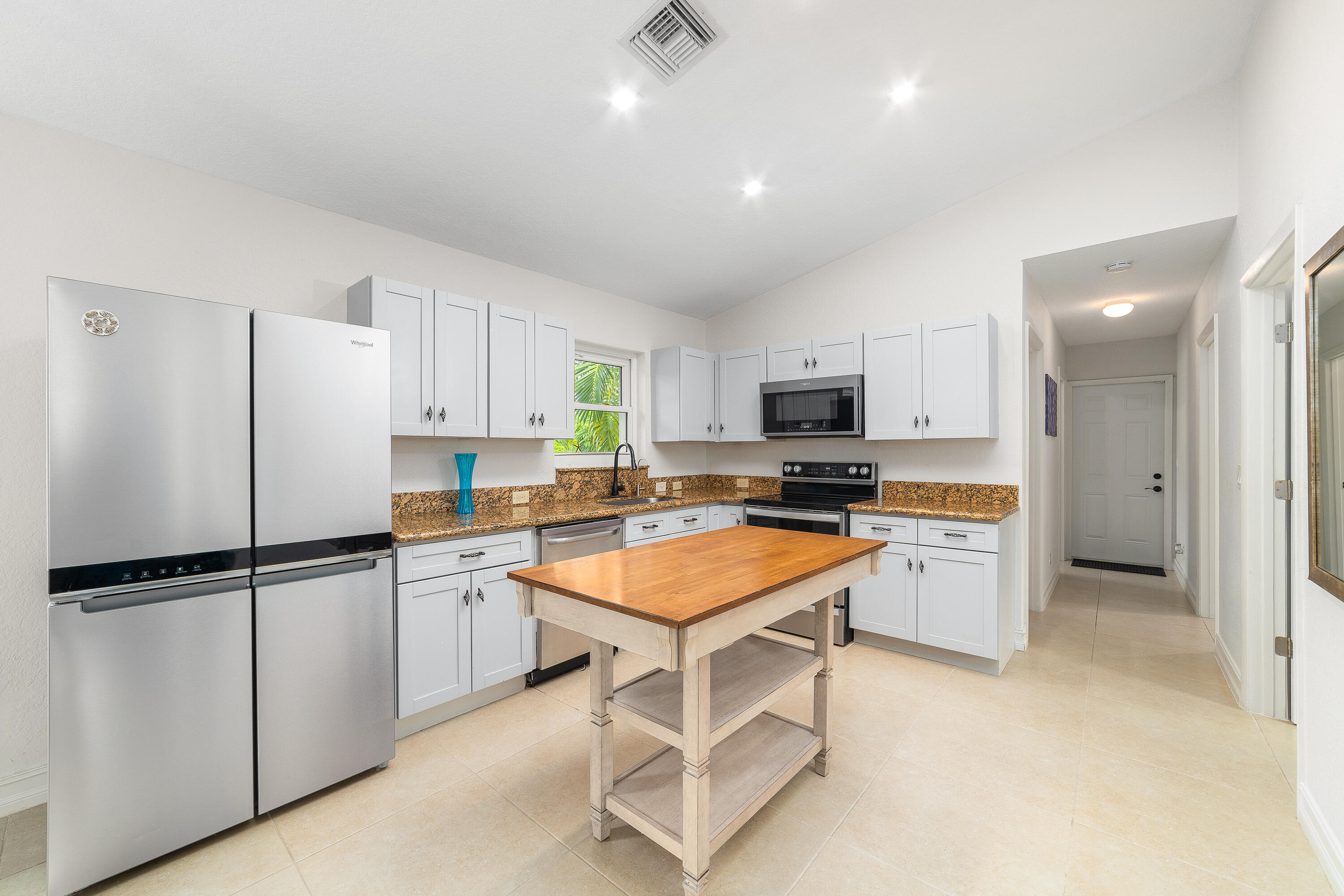 Kitchen with white cabinets, stainless steel appliances, brown countertops, and a central wooden worktable.