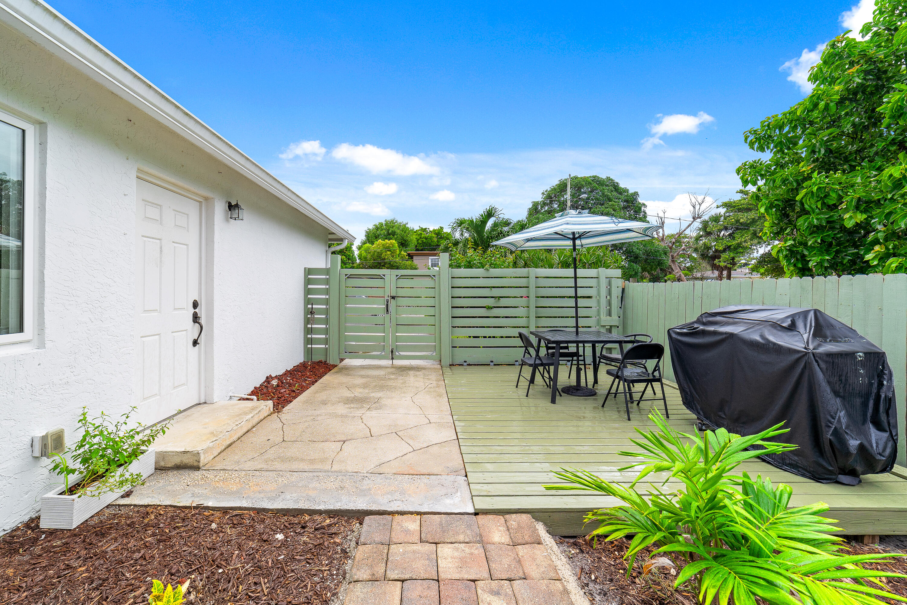 Fenced patio with a green deck, umbrella-shaded dining set, and covered grill.