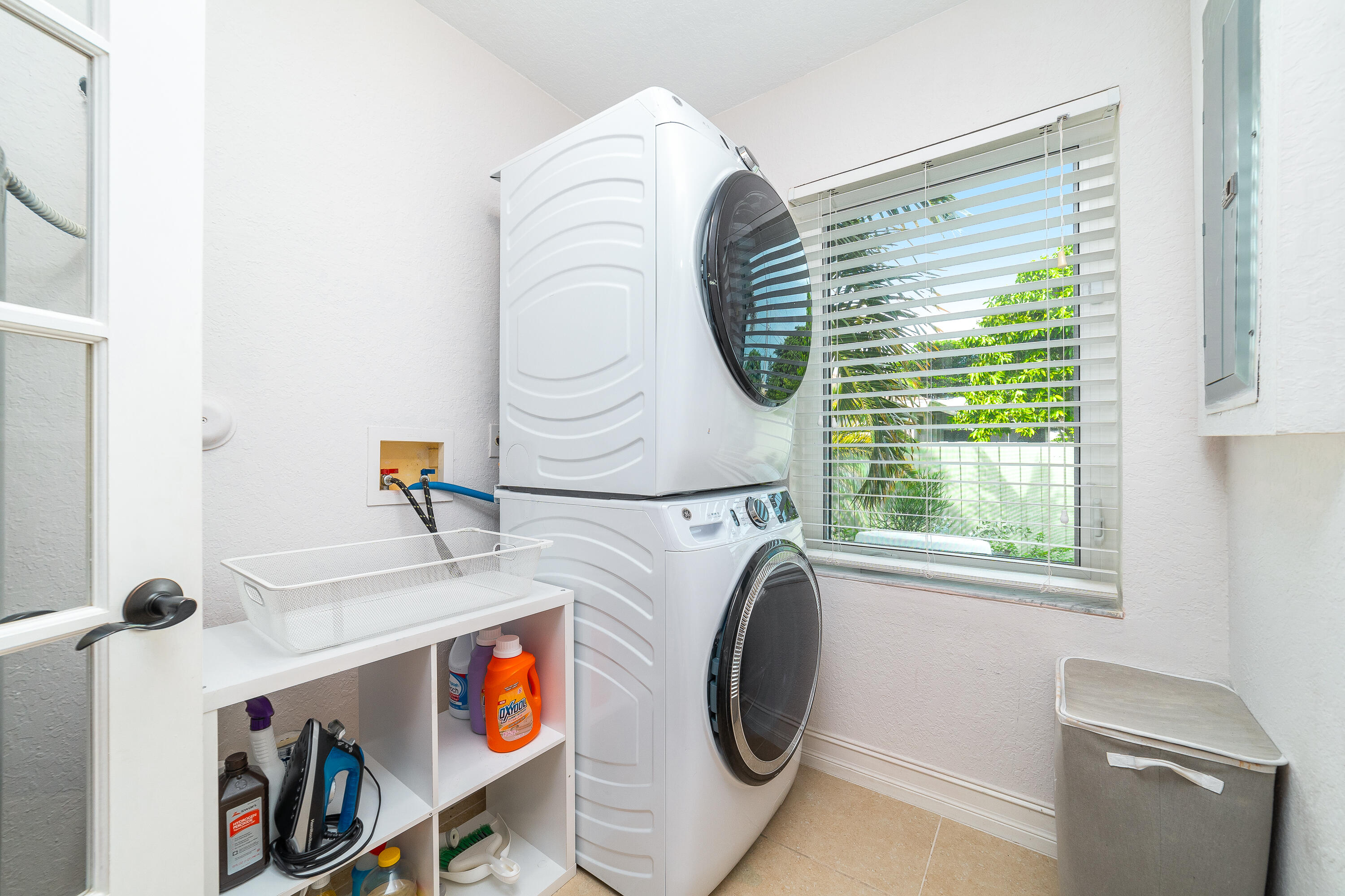 Laundry room with stacked front-load washer and dryer beside a window overlooking greenery.