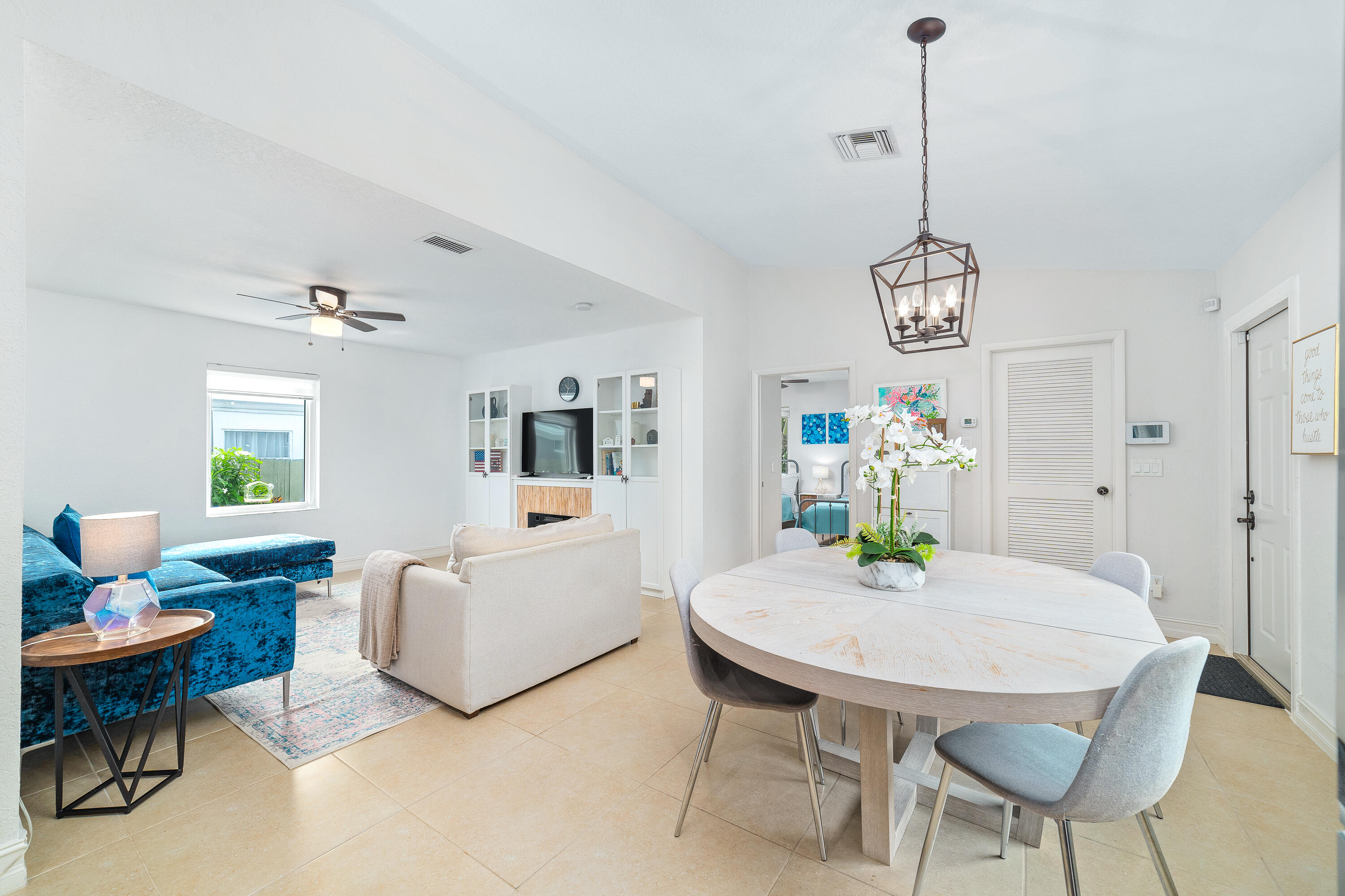 Open-plan living and dining room with a blue sectional, white oval table, and built-in TV cabinets.