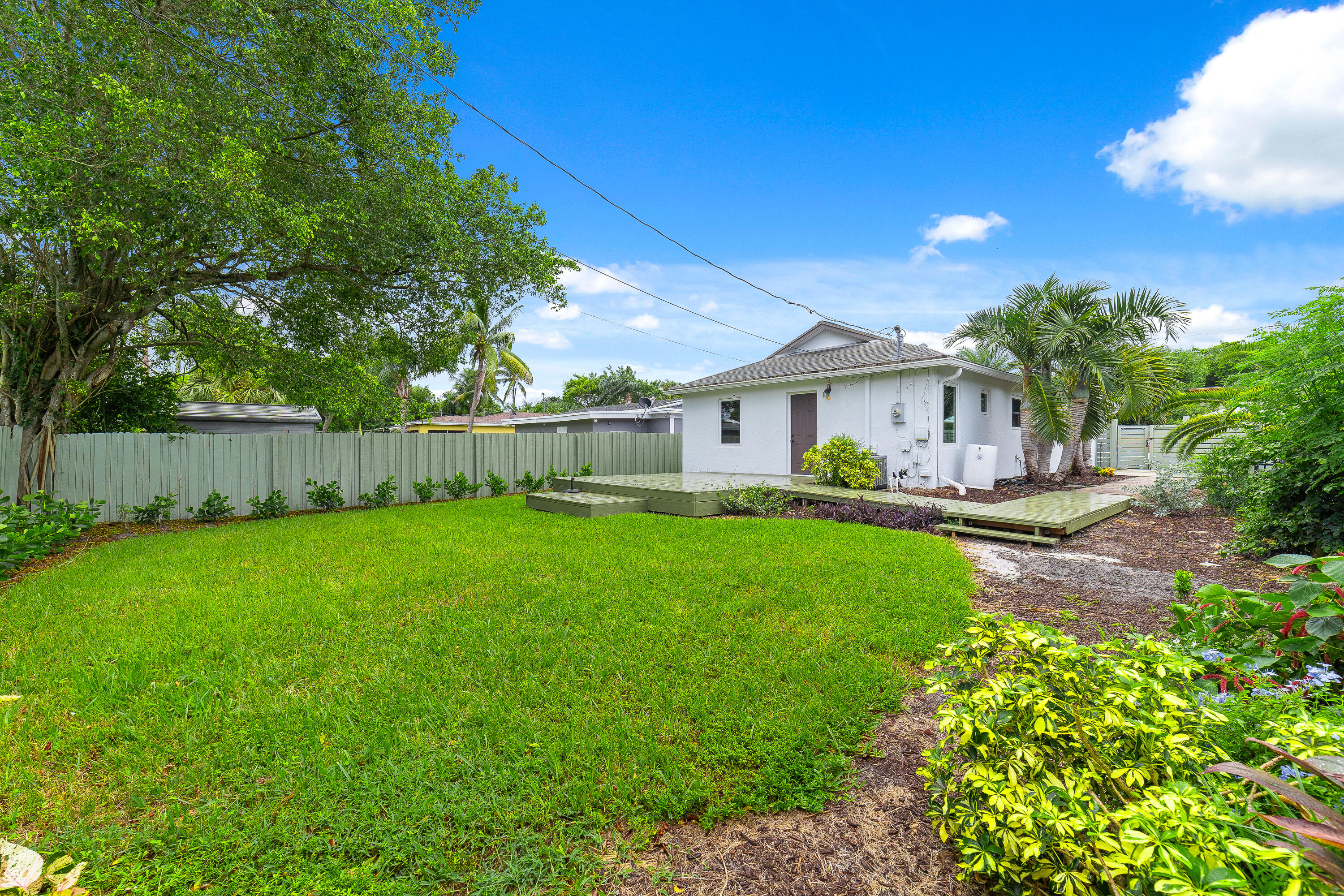 White house viewed from the backyard, with a raised deck, broad lawn, and tropical landscaping.