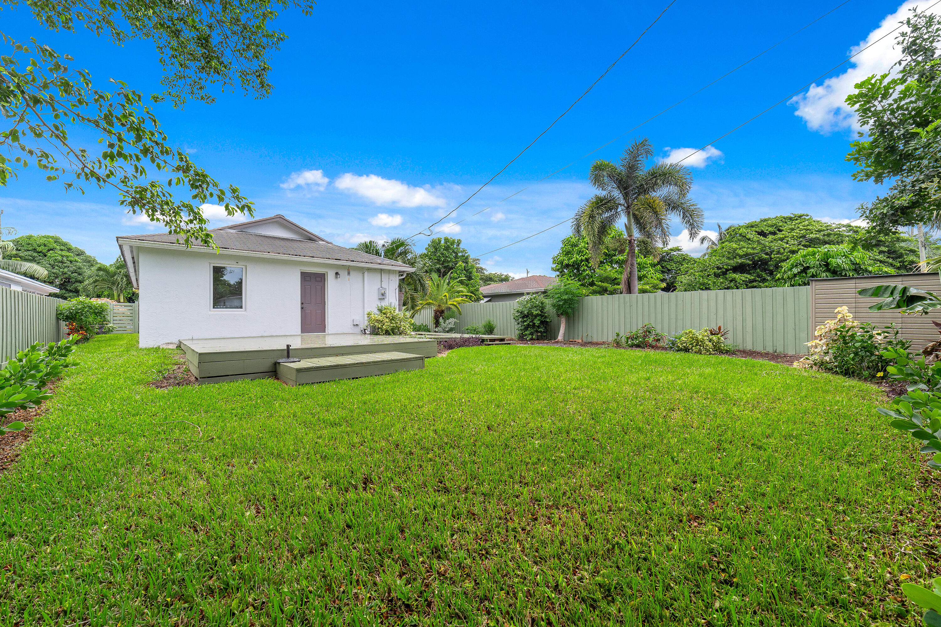 White home’s rear deck overlooks a broad lawn and fenced tropical backyard.