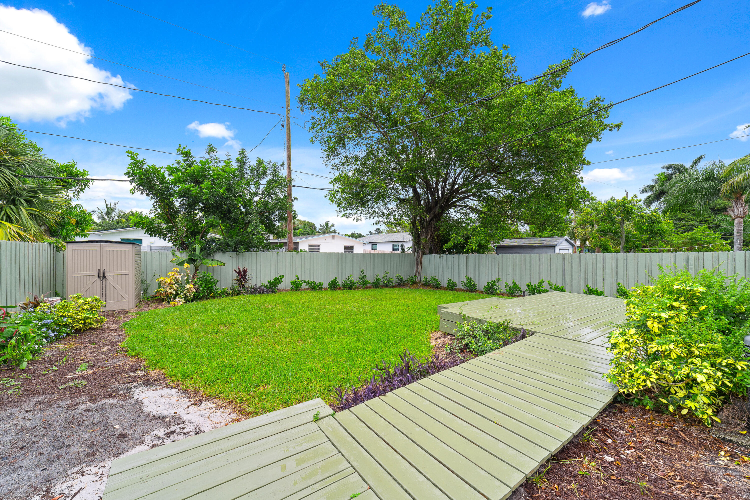 Backyard with a raised wooden deck, green lawn, privacy fence, and large shade tree.