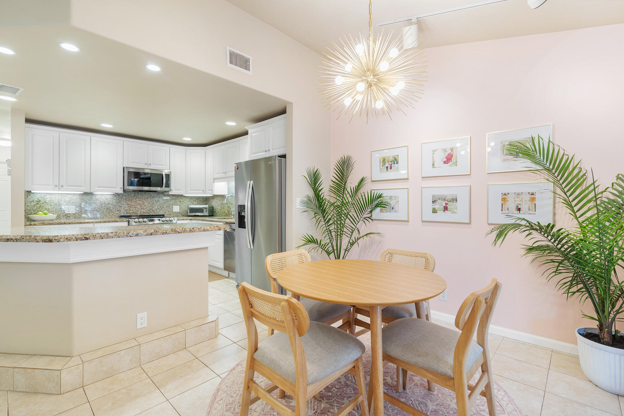 Open kitchen and dining area with white cabinets, stainless appliances, and a round table beneath a starburst chandelier.