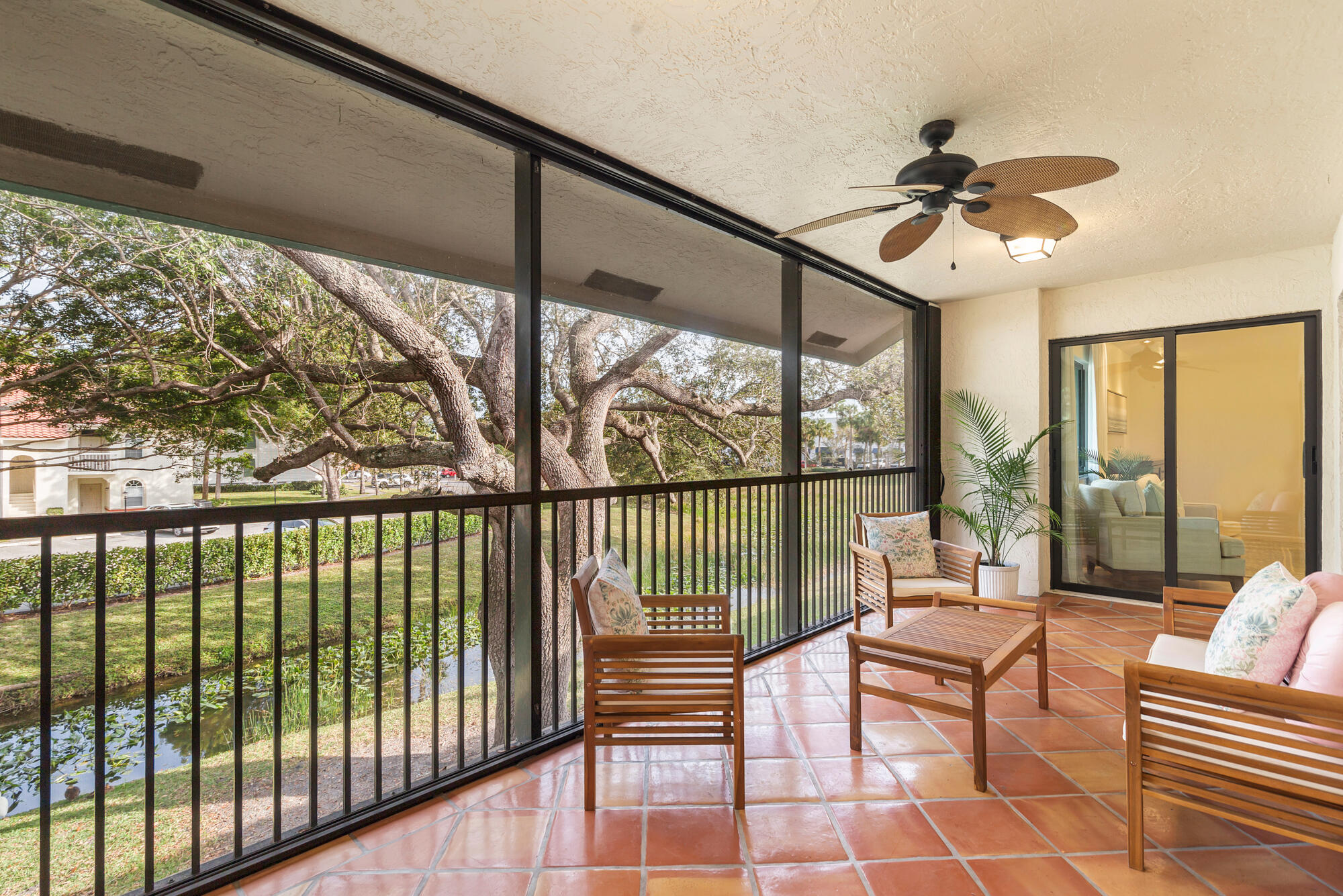 Screened patio with terracotta tile and wooden seating overlooking a tree-lined waterway.