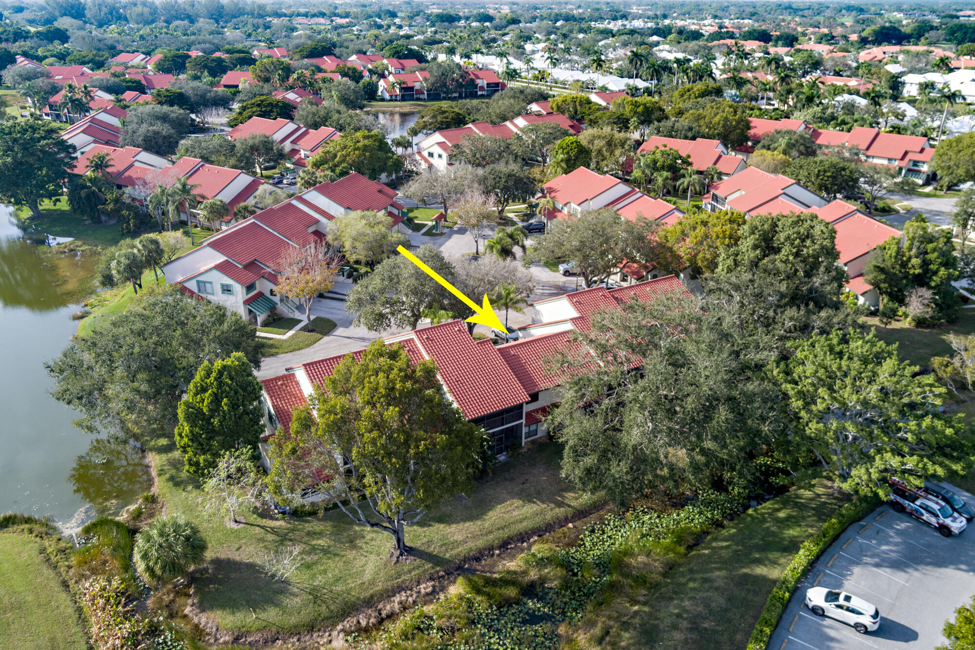 Aerial view of the condo community, with a yellow arrow marking the red-tile-roof unit beside a pond.