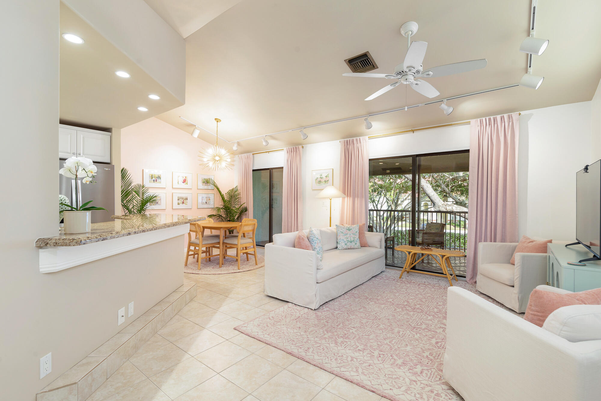 Furnished living room with white sofas, blush curtains, and sliding doors to a tree-lined balcony.