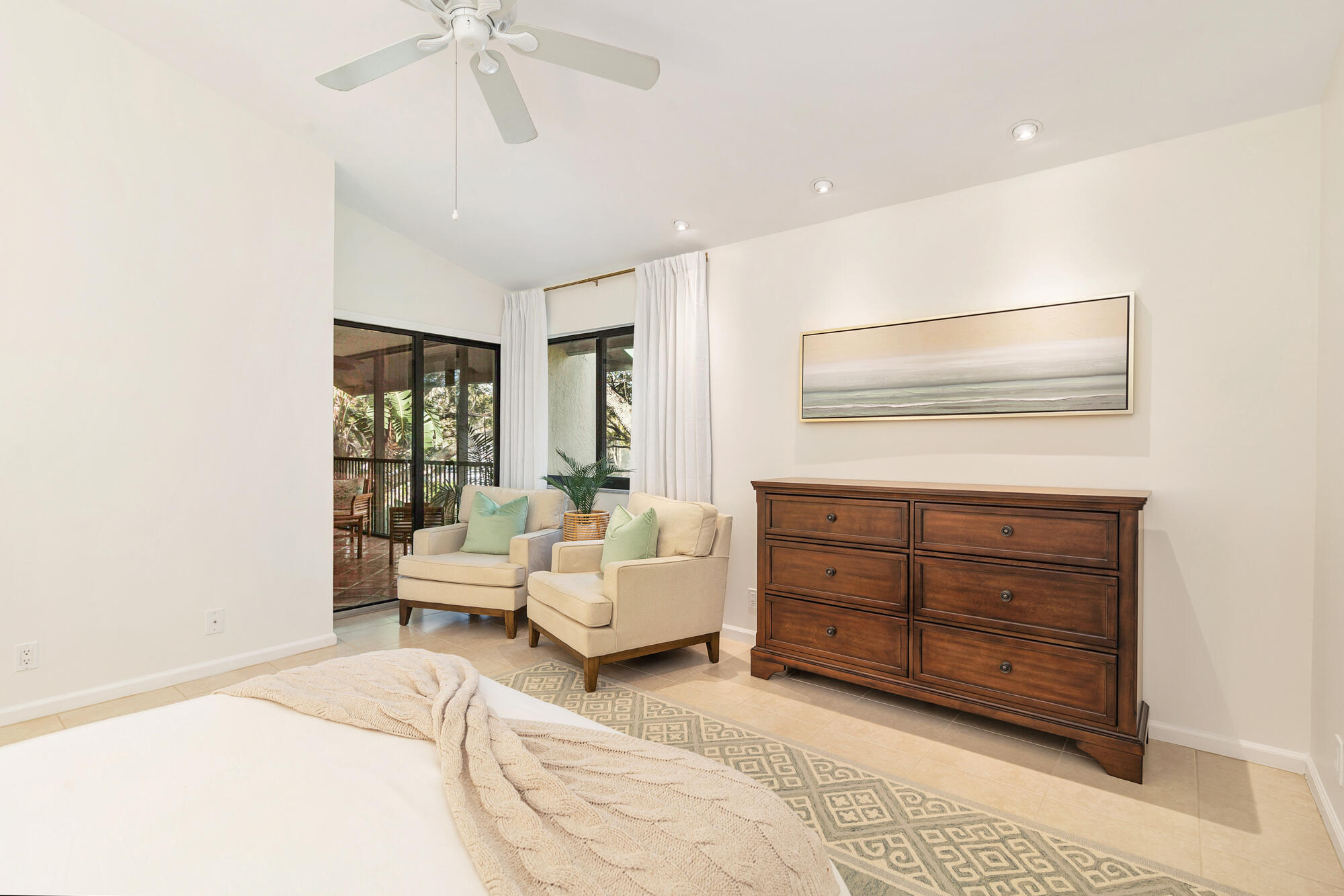Furnished bedroom with cream armchairs beside sliding glass doors and a dark wood dresser.