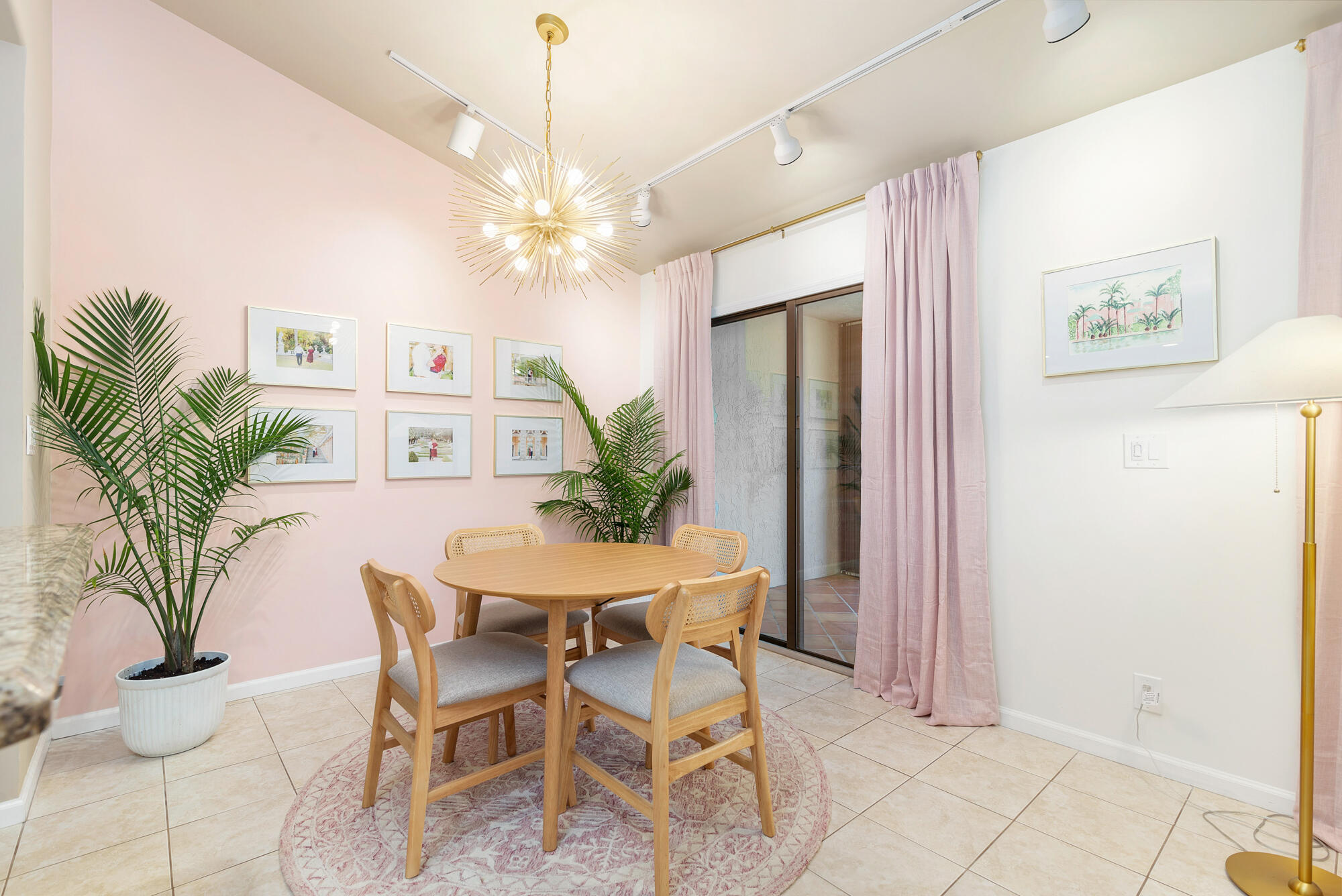 Dining area with a round wooden table, pink curtains, potted palms, and a starburst pendant light.