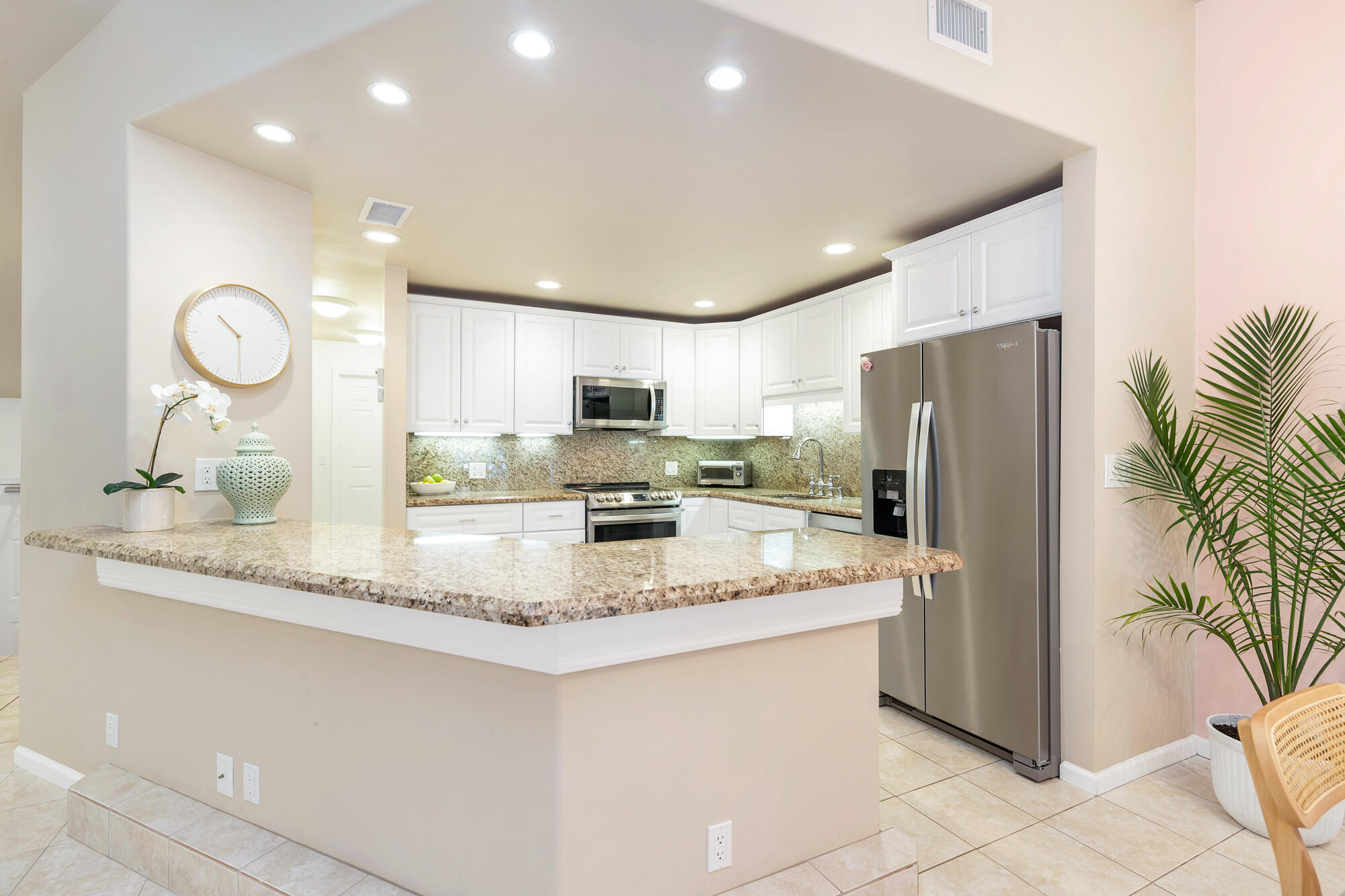 Kitchen with a large granite breakfast bar, white cabinets, and stainless steel appliances.