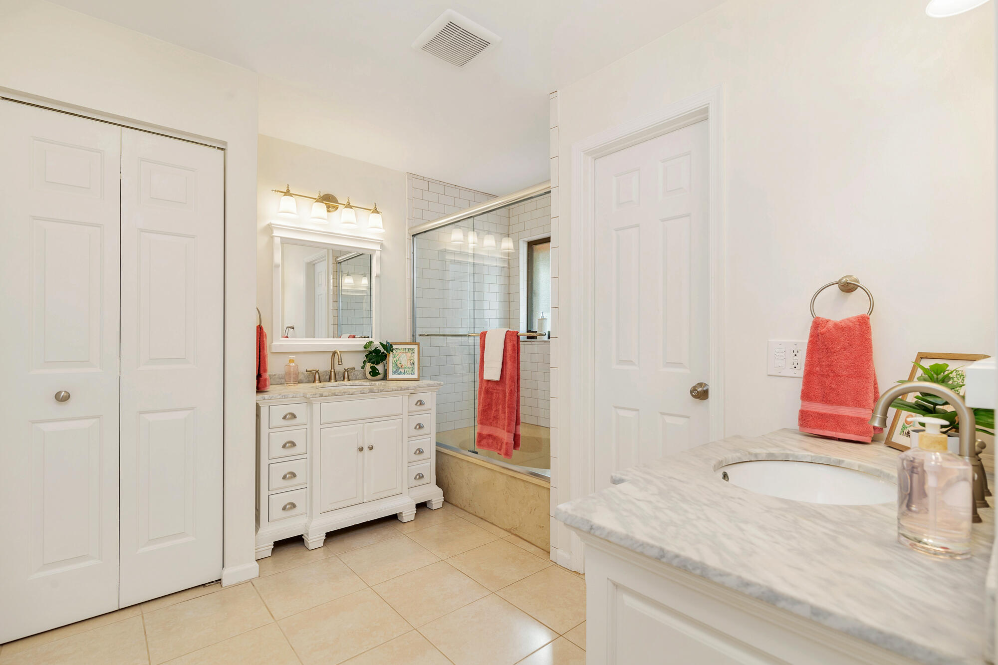 Bathroom with white vanities, marble counters, and a glass-enclosed subway-tile shower.