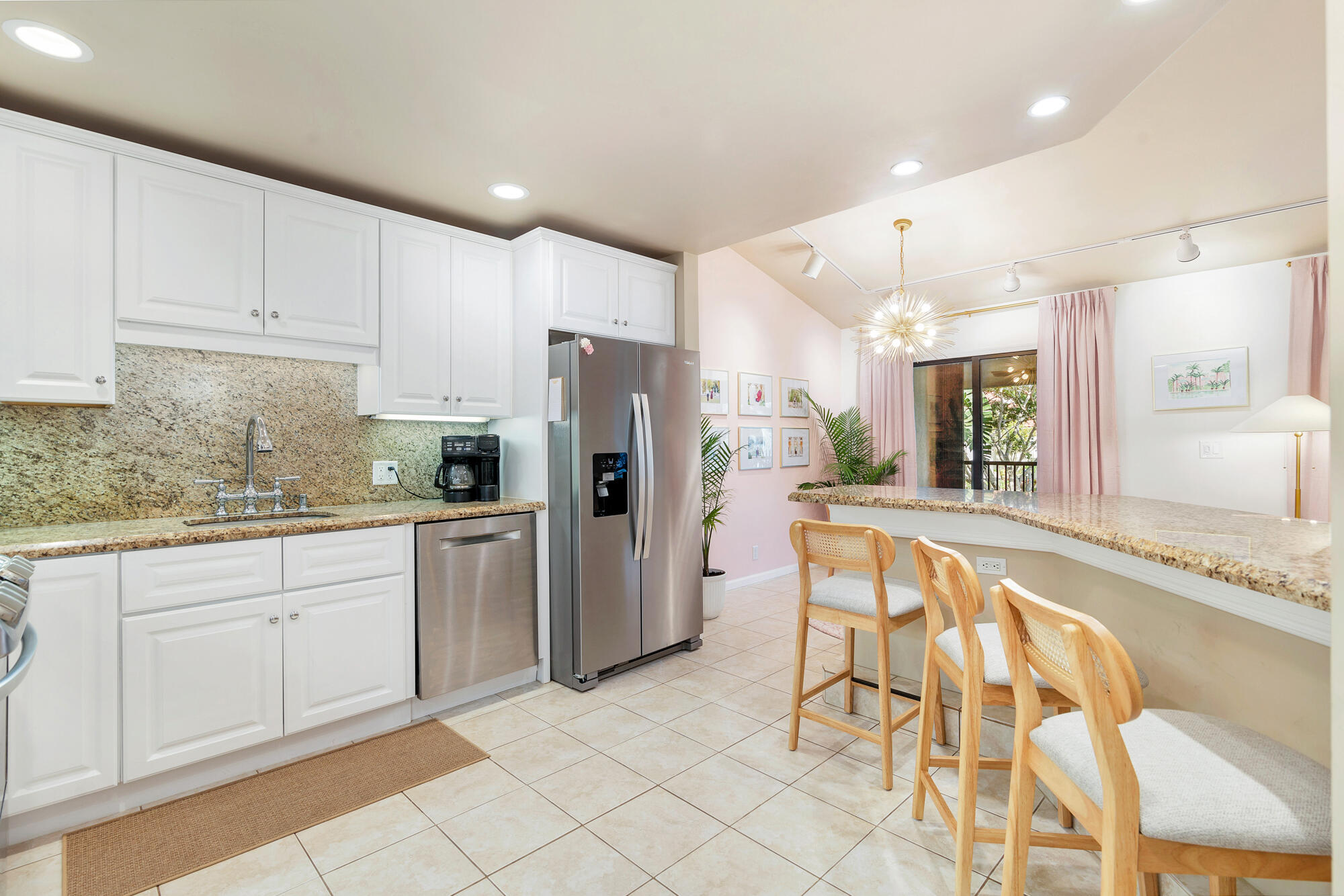 Kitchen with white cabinets, stainless steel appliances, granite counters, and a breakfast bar with wooden chairs.