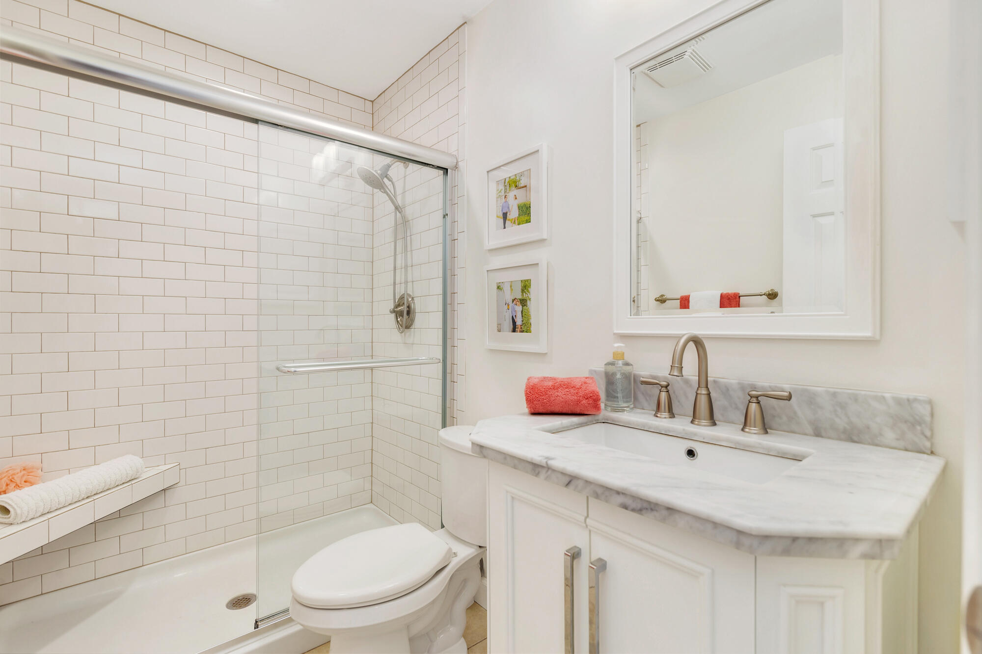 Bathroom with a glass-enclosed subway-tile shower and marble vanity accented by coral towels.