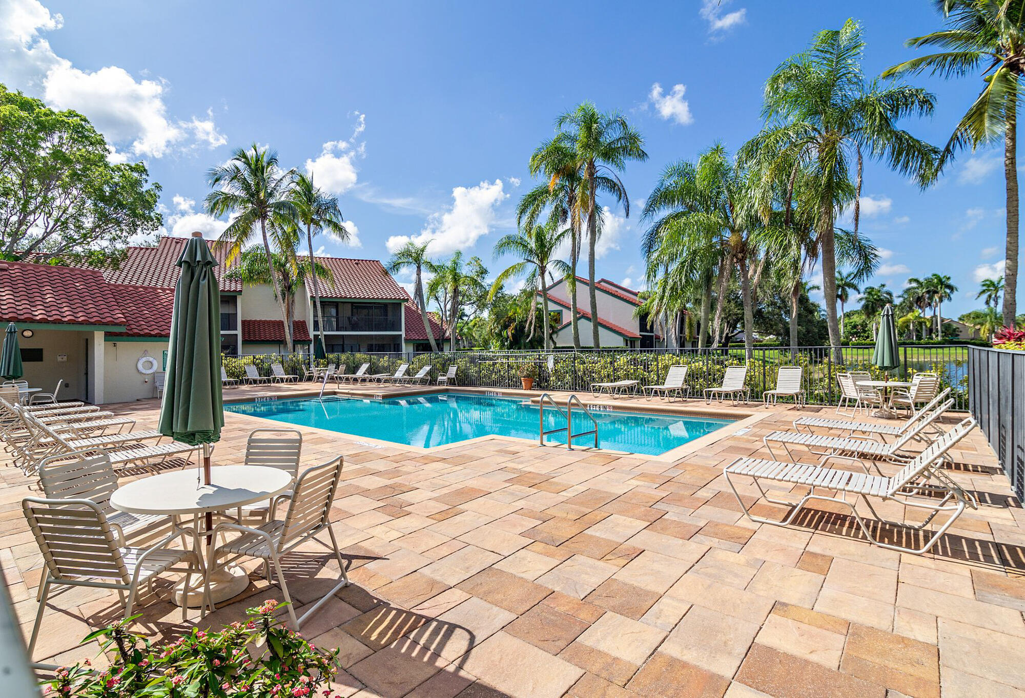 Outdoor community pool with lounge chairs, palm trees, and tiled-roof buildings.
