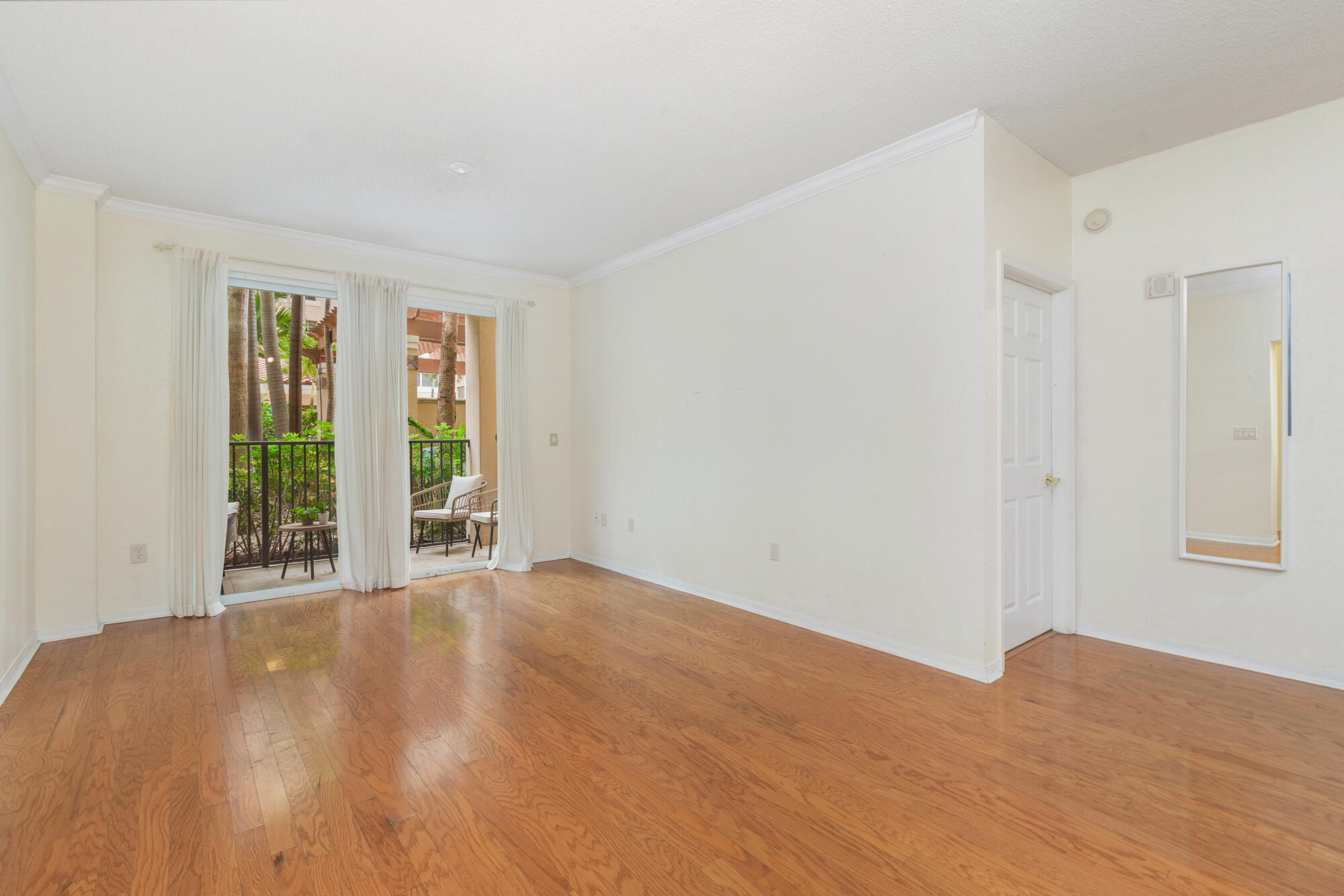 Empty living room with hardwood floors and sliding glass doors opening to a furnished patio.