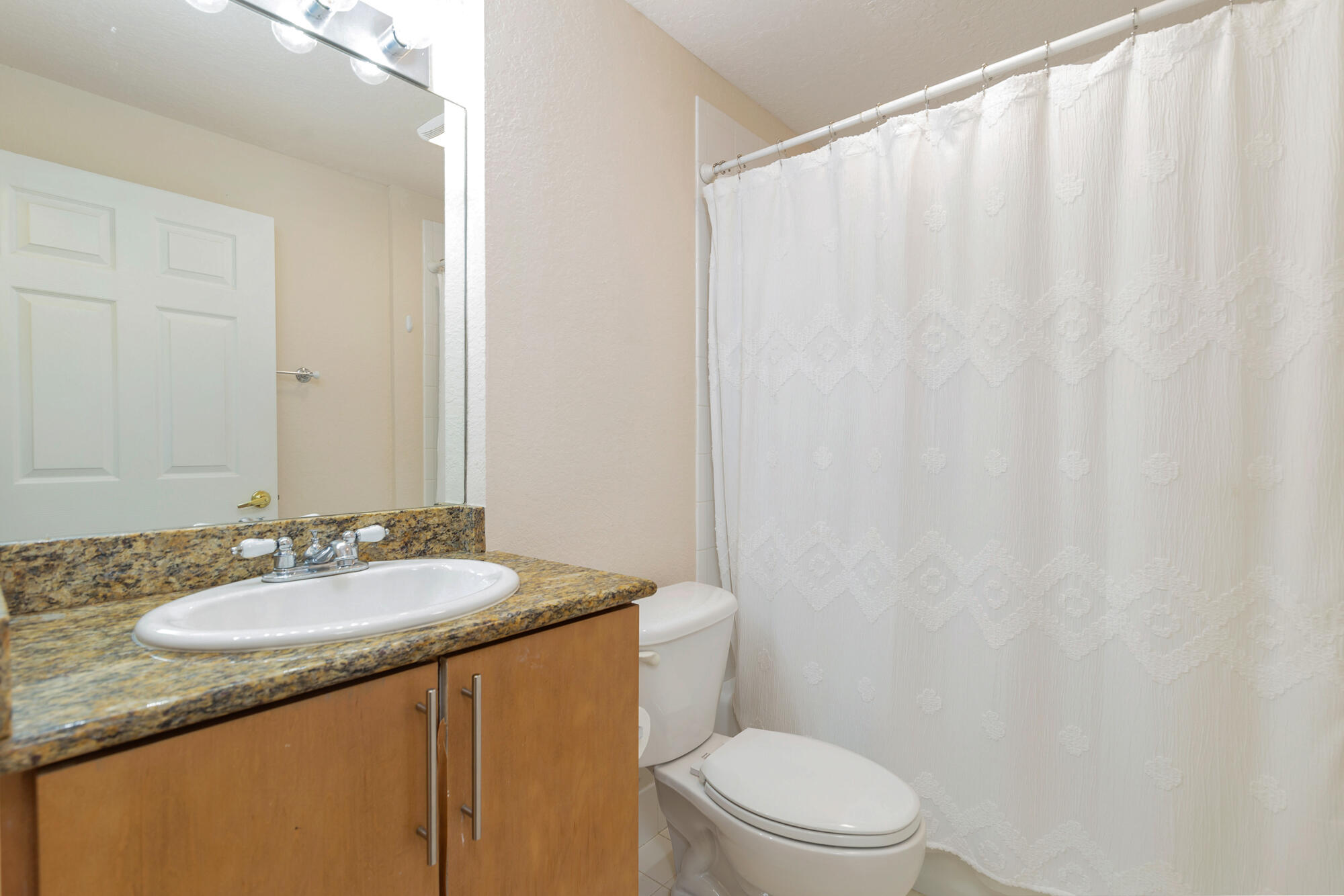 Bathroom with a granite vanity, white sink, toilet, and patterned shower curtain.