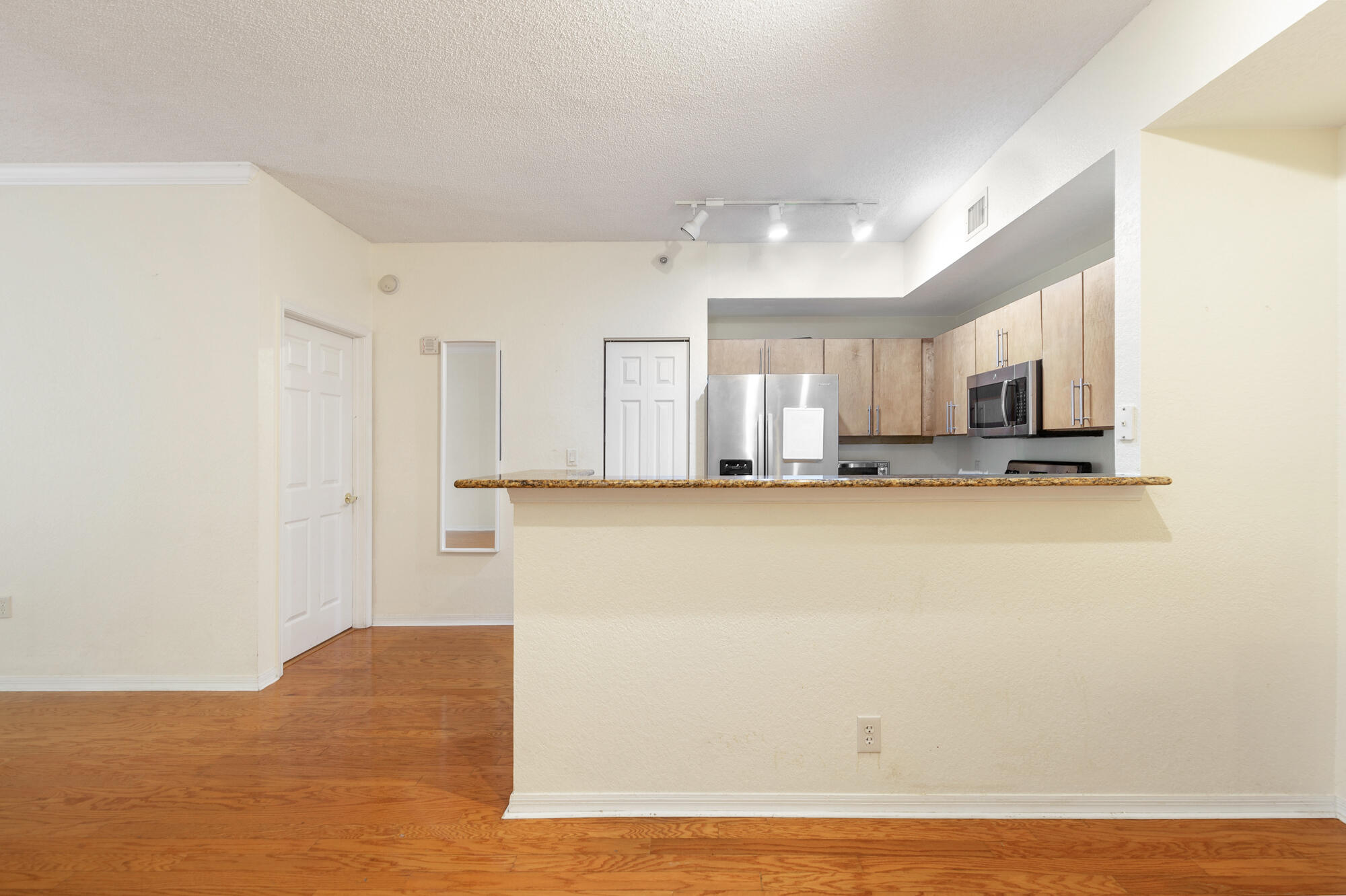 Open condo kitchen with a granite breakfast bar, light wood cabinets, and stainless steel appliances.