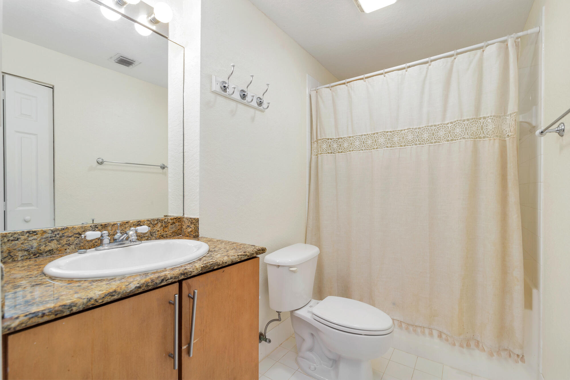 Bathroom with a granite vanity, oval sink, toilet, and cream lace-trimmed shower curtain.