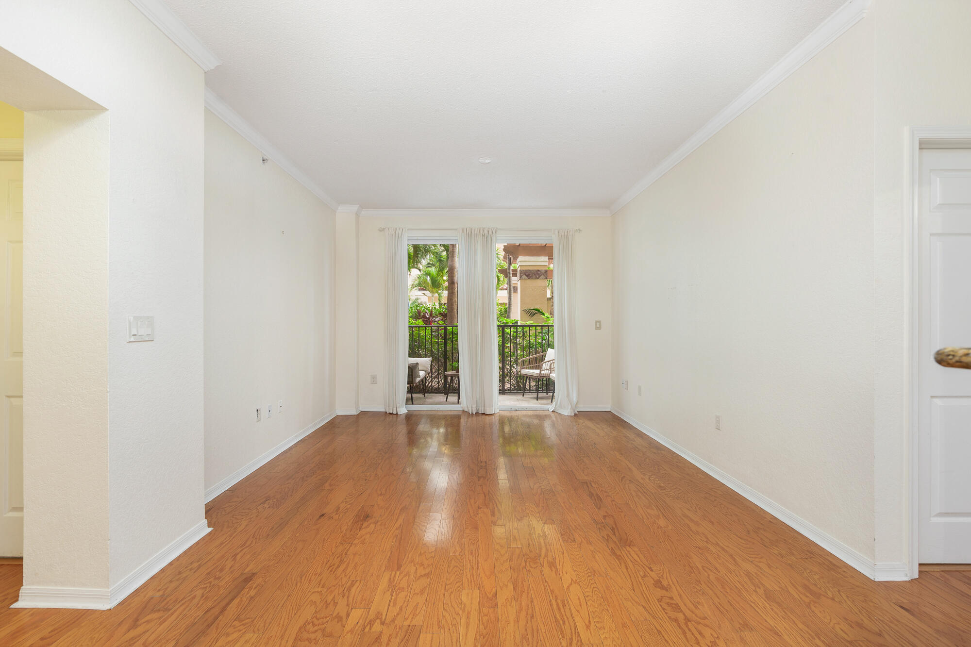 Empty living room with hardwood floors and sliding glass doors to a leafy patio.