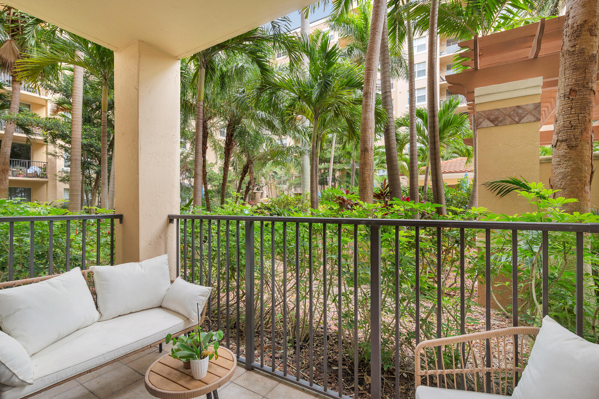 Covered patio with wicker seating overlooking a lush courtyard filled with palm trees.