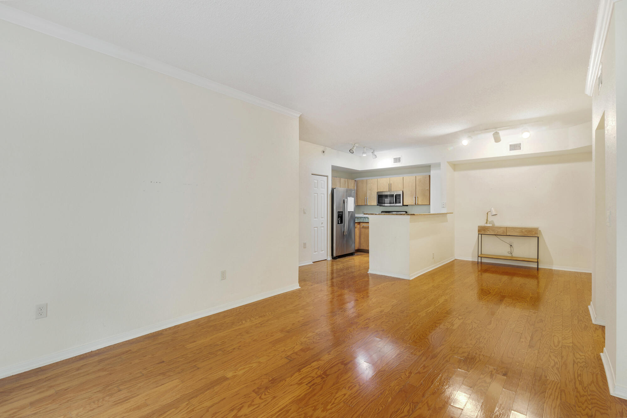 Open-plan living area with glossy hardwood floors, a breakfast bar, and a light wood kitchen.
