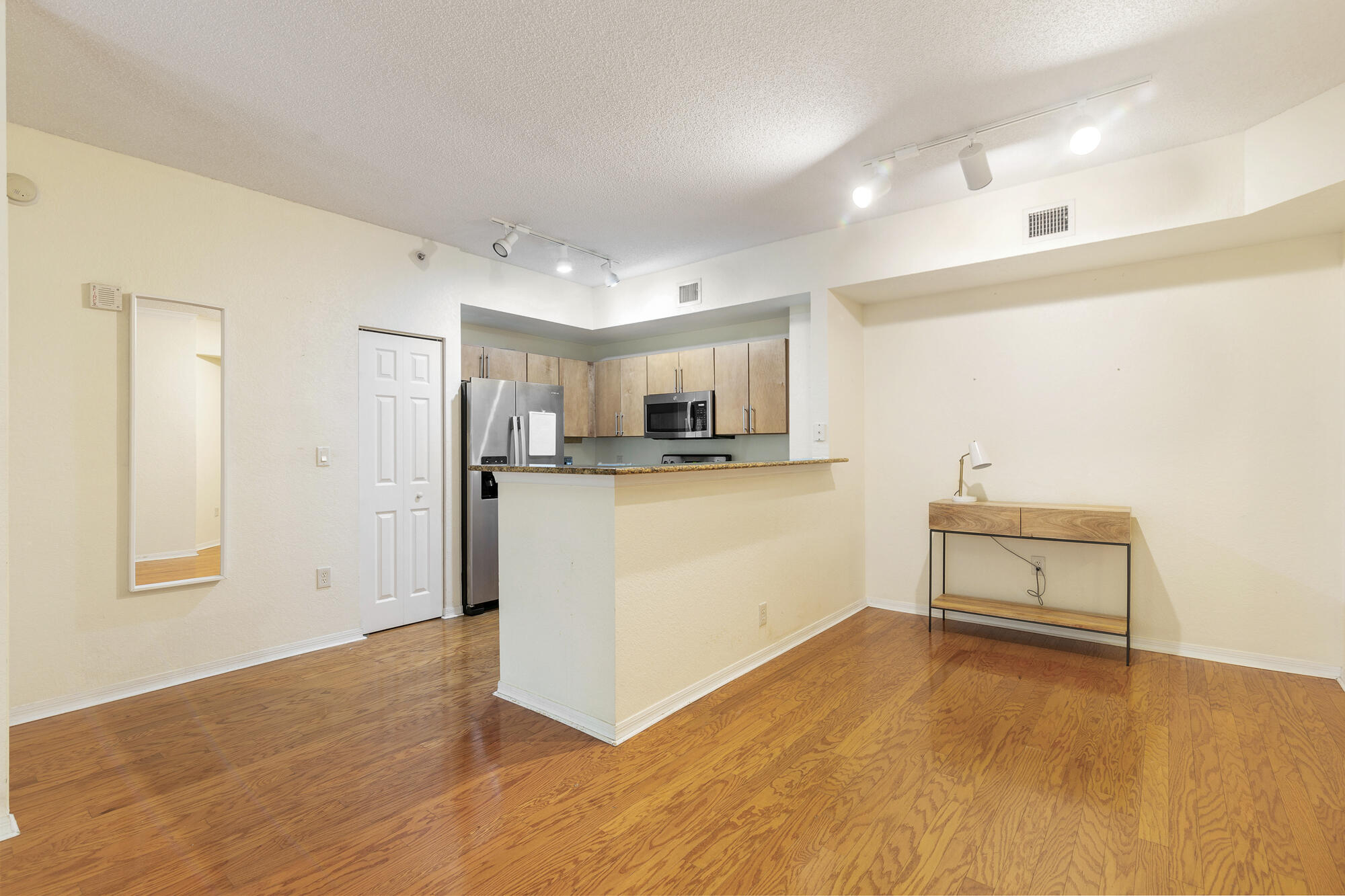 Open-plan living area with hardwood floors, a granite kitchen bar, and stainless steel appliances.