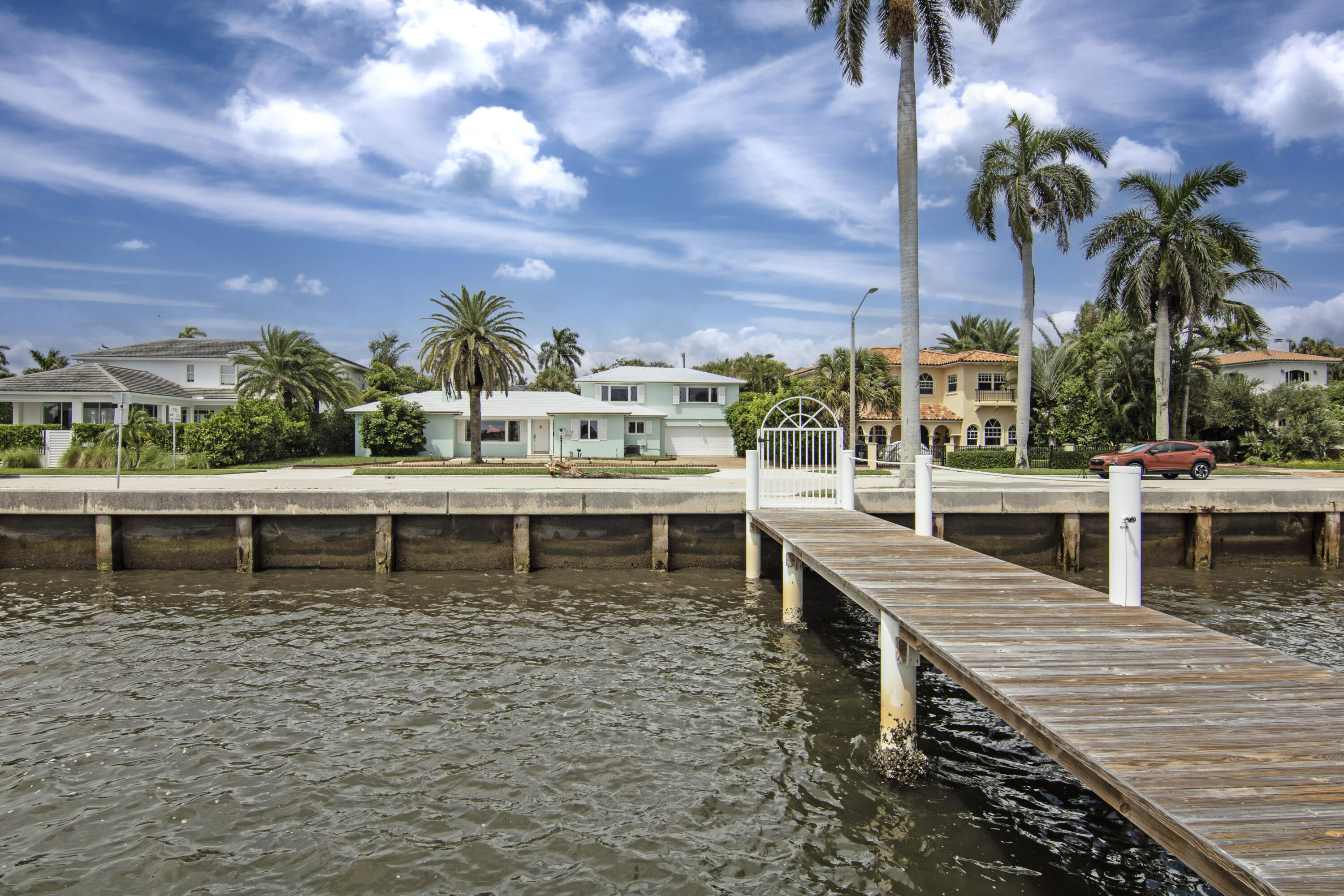 Waterfront homes and palm trees across a canal, viewed from a wooden dock.
