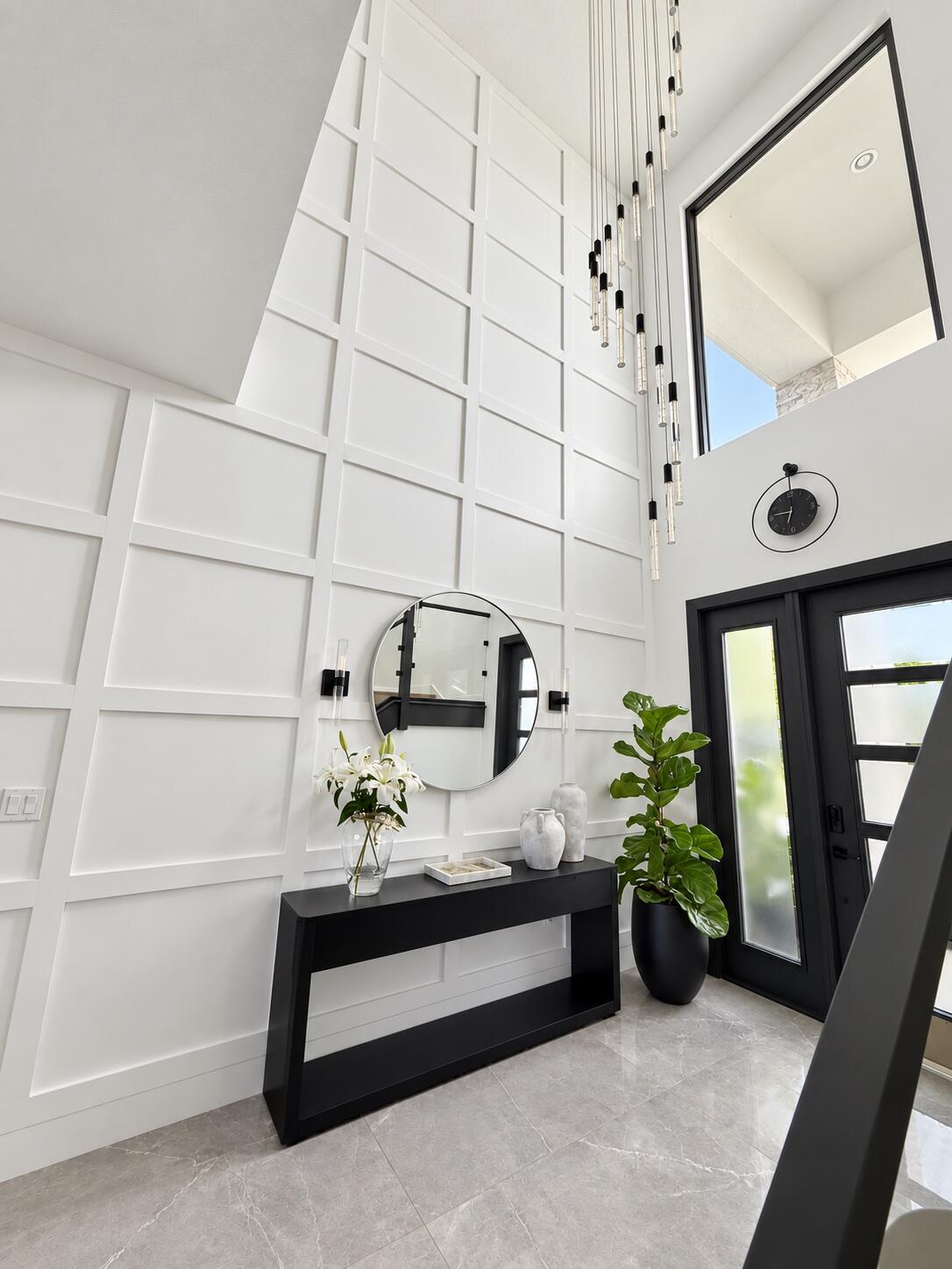 Double-height entry foyer with geometric white walls, a black console table, round mirror, and glass pendant lights.
