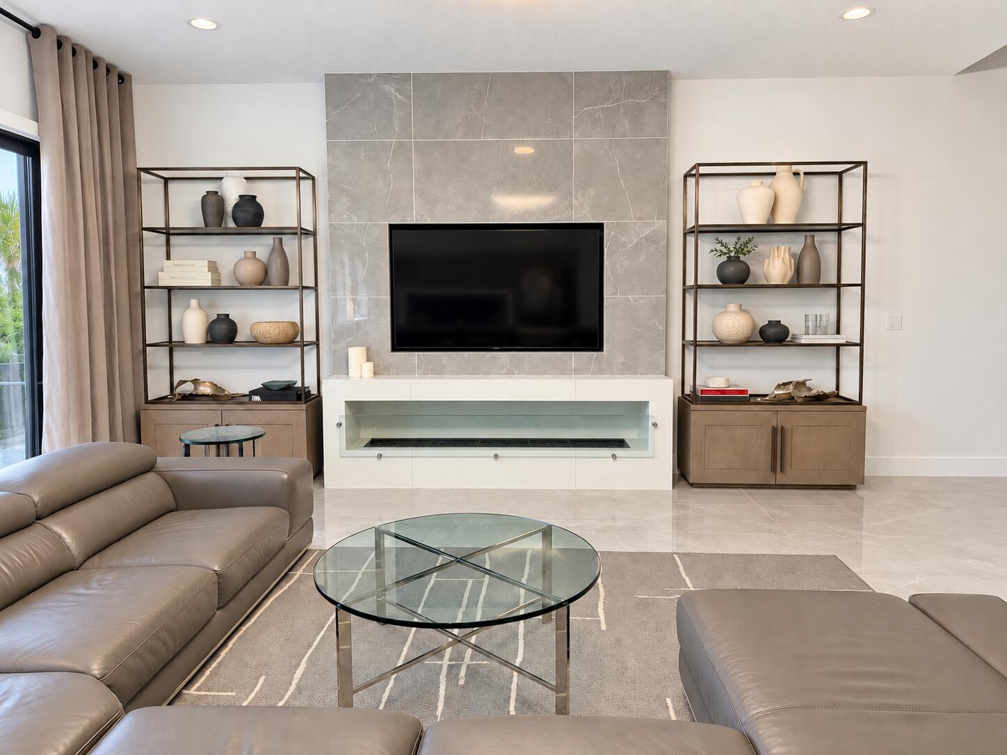 Furnished living room with taupe leather seating, a tiled TV wall, and a linear fireplace.