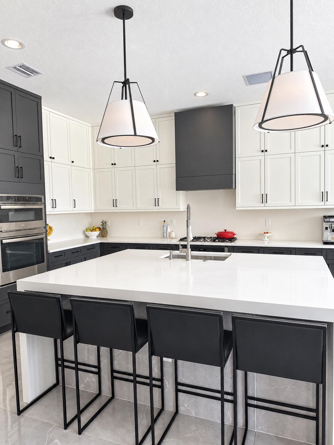 Modern kitchen with a large white island, four black stools, and white and charcoal cabinetry.