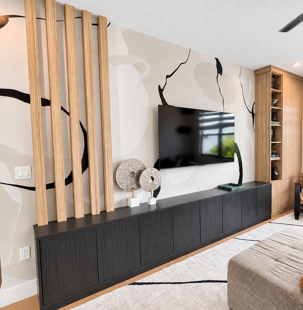 Living room media wall with a mounted television, dark cabinet, abstract mural, and vertical wood slats.