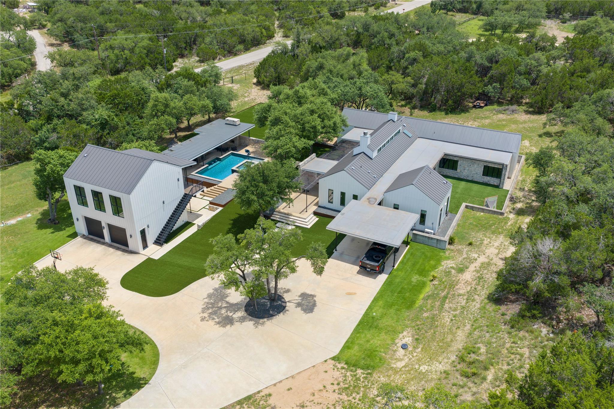 Aerial view of a modern white home with a pool, detached garage, and broad concrete driveway.