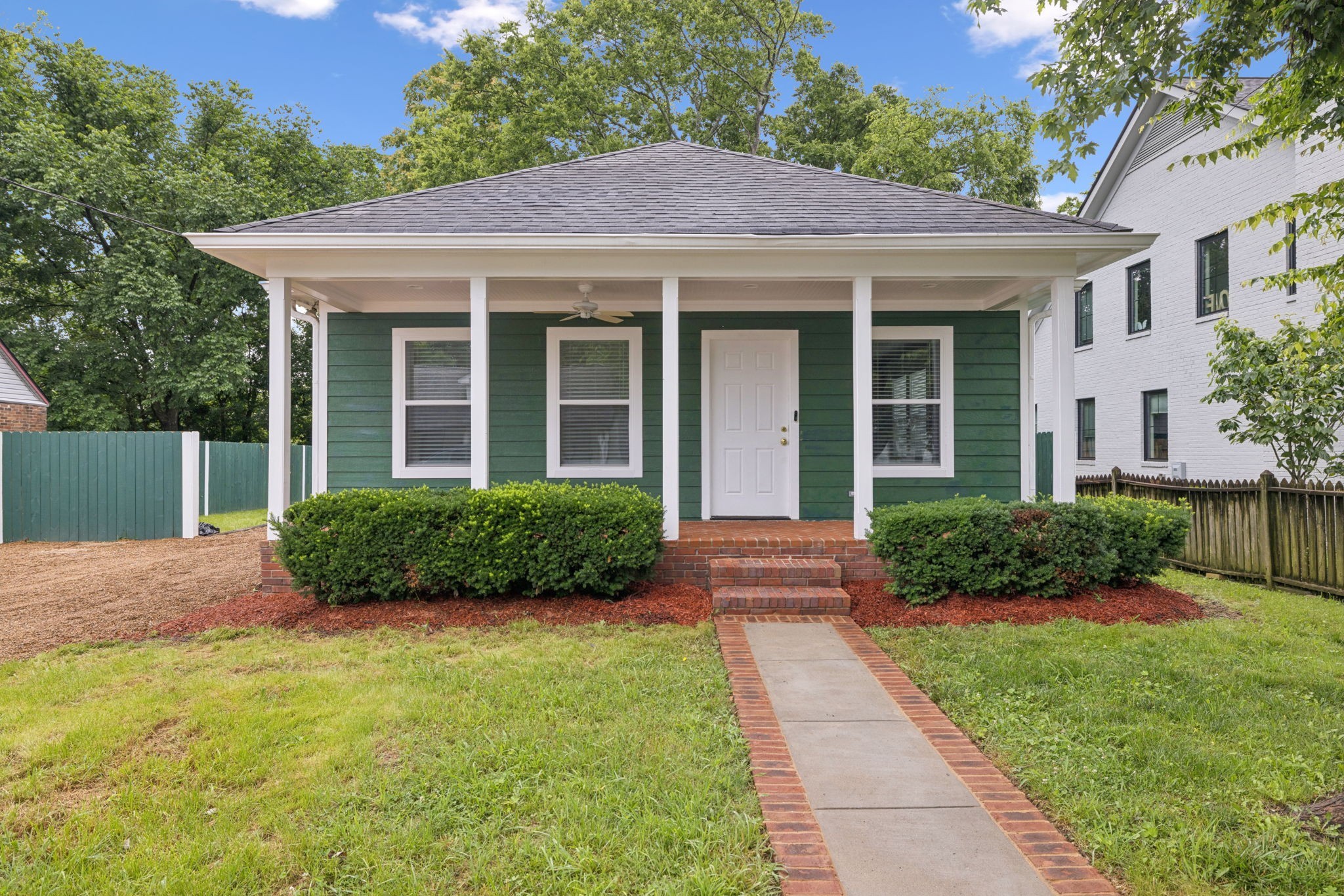 Green house with a broad covered porch, white trim, and a brick-edged walkway.