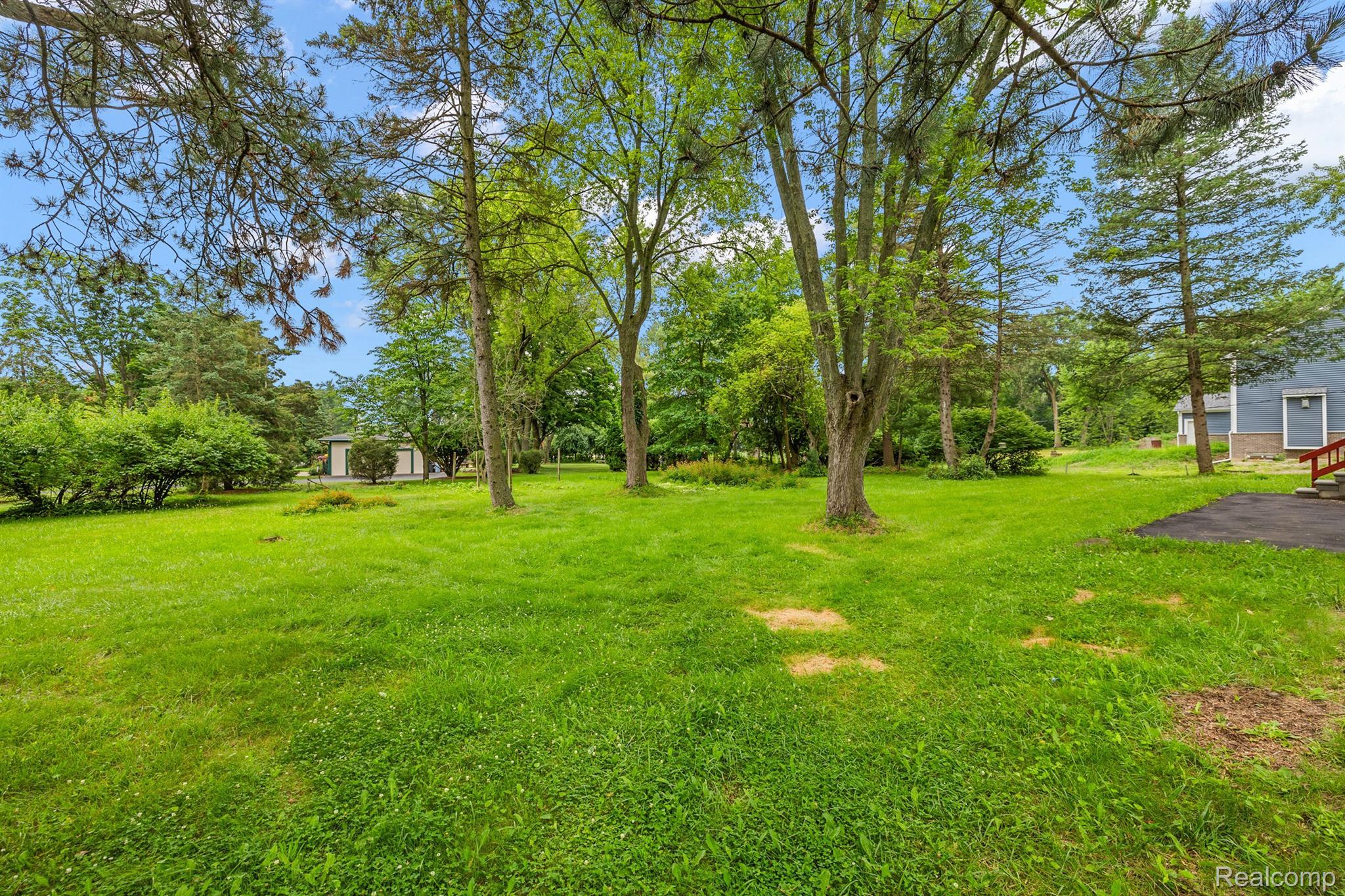 Tree-lined grassy backyard with a detached outbuilding and part of a blue-sided house.