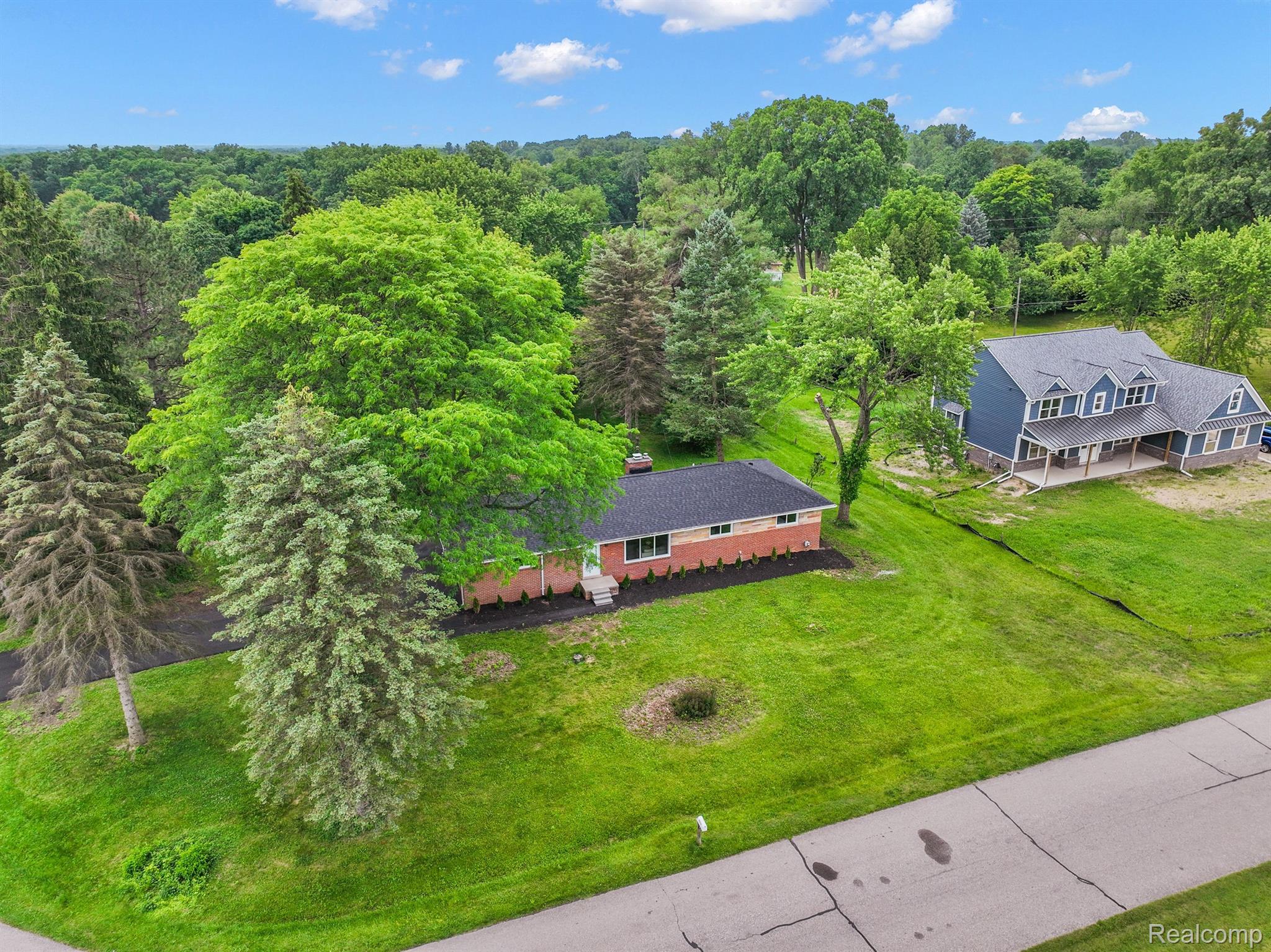 Aerial view of a red brick ranch house on a spacious, tree-lined lawn.