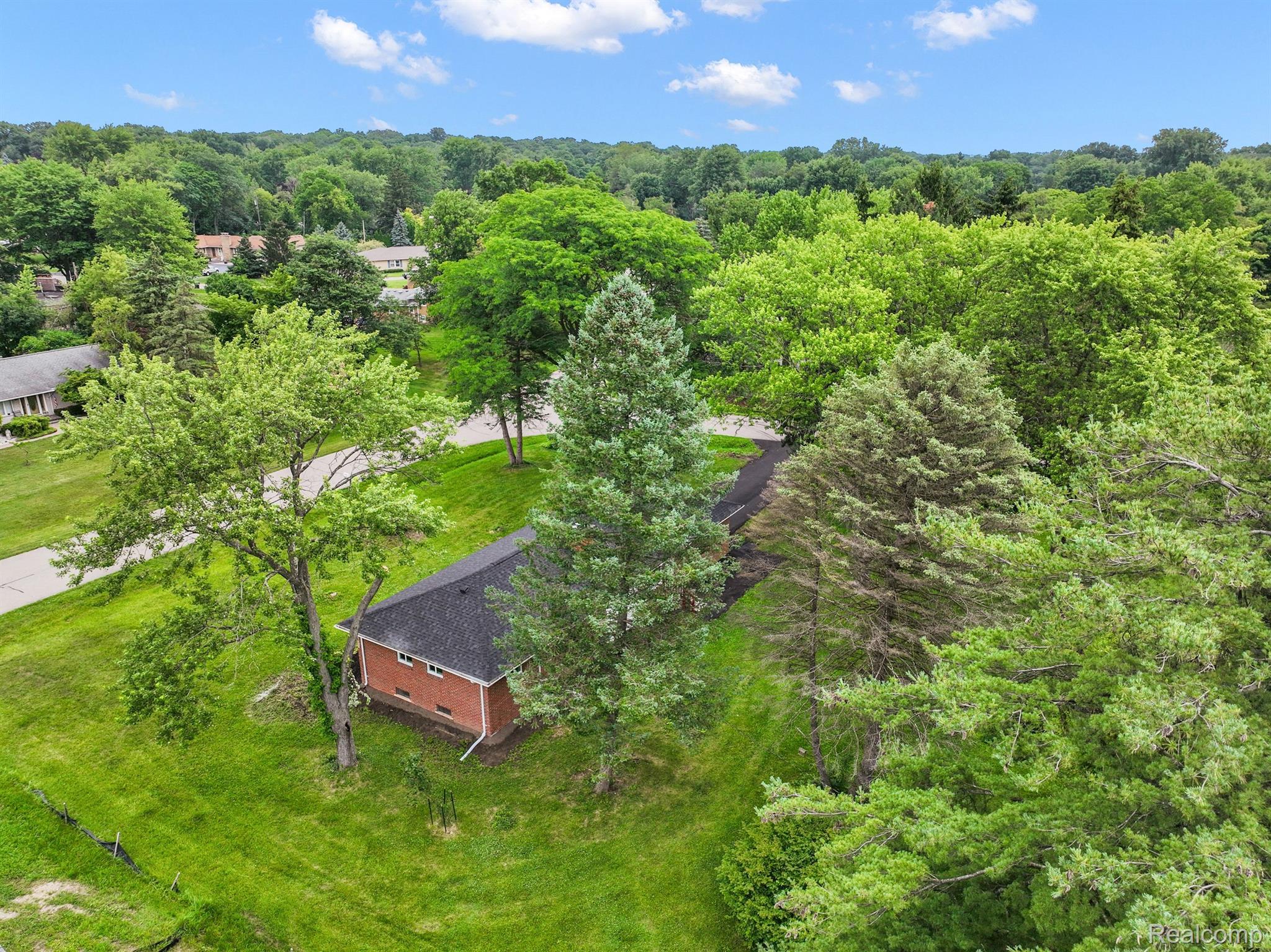 Aerial view of a brick house nestled among mature trees on a spacious green lot.
